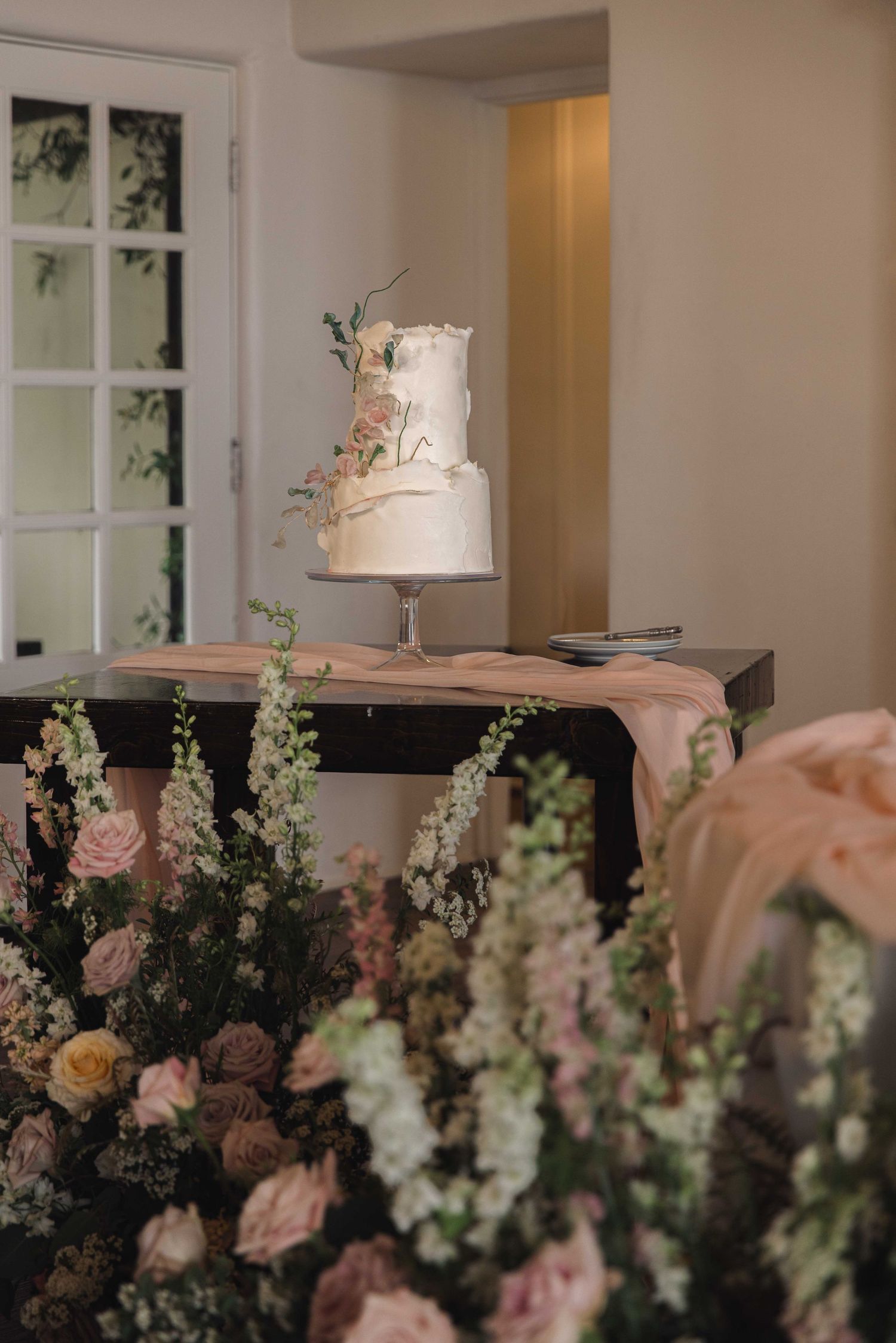 Elegant white wedding cake displayed with lush pink and peach floral arrangements.
