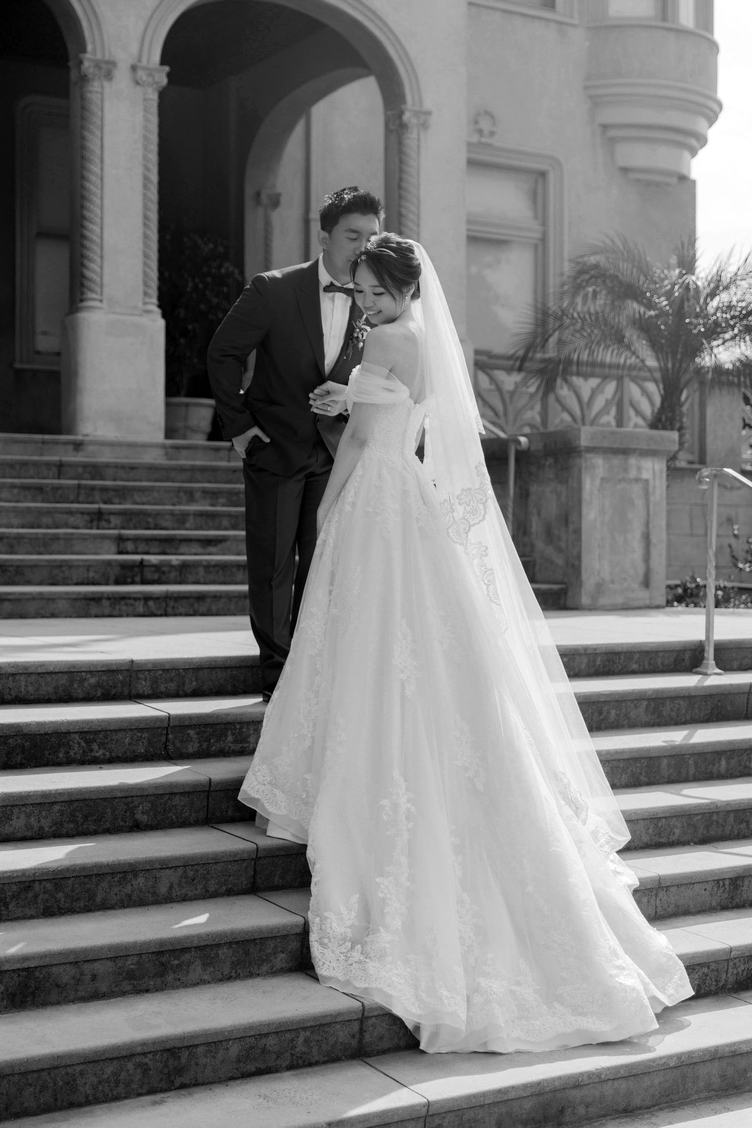 A bride in a white ballgown descends ornate stone steps at a classic venue.