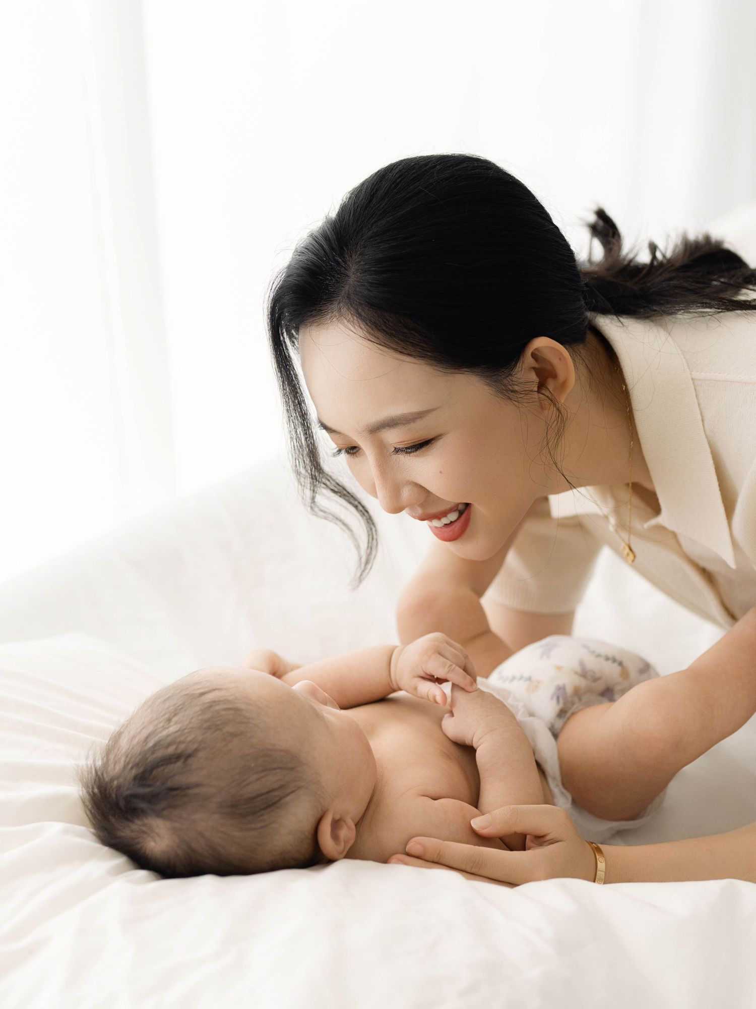 Parent bonding with baby during intimate photoshoot on white bedding.