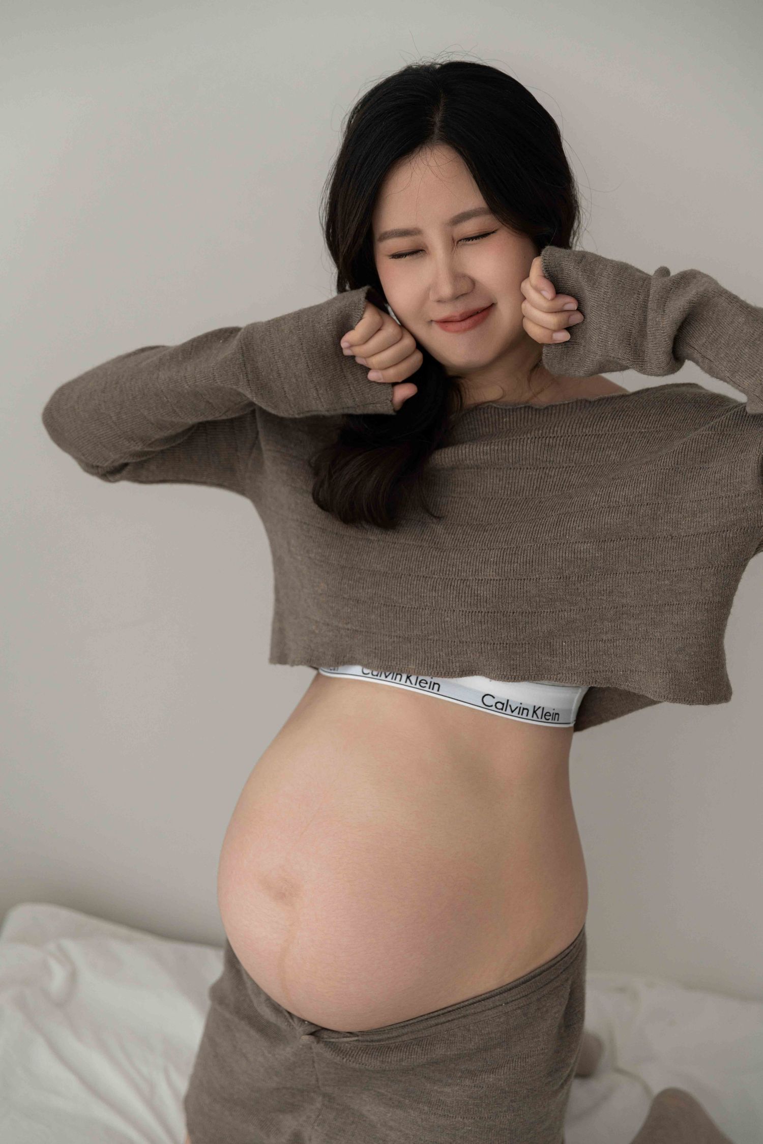 A series of maternity photos showing a pregnant belly in a brown sweater against a light background.