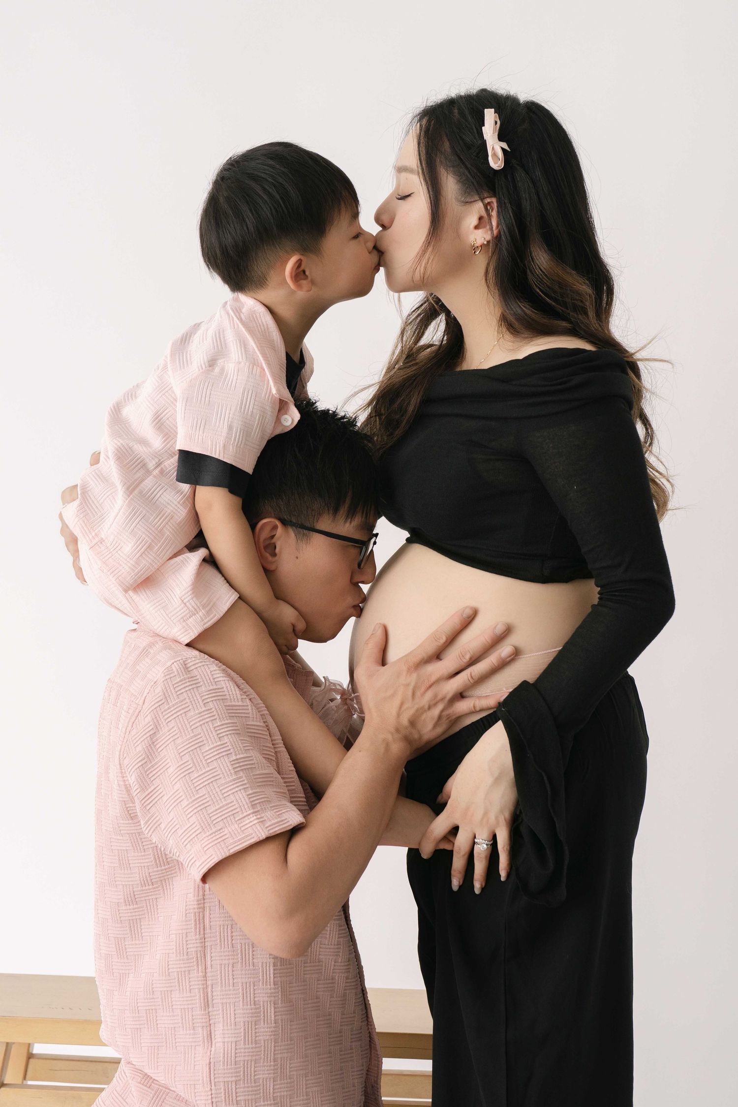 Family maternity photo showing tender moment with child kissing mother's pregnant belly.