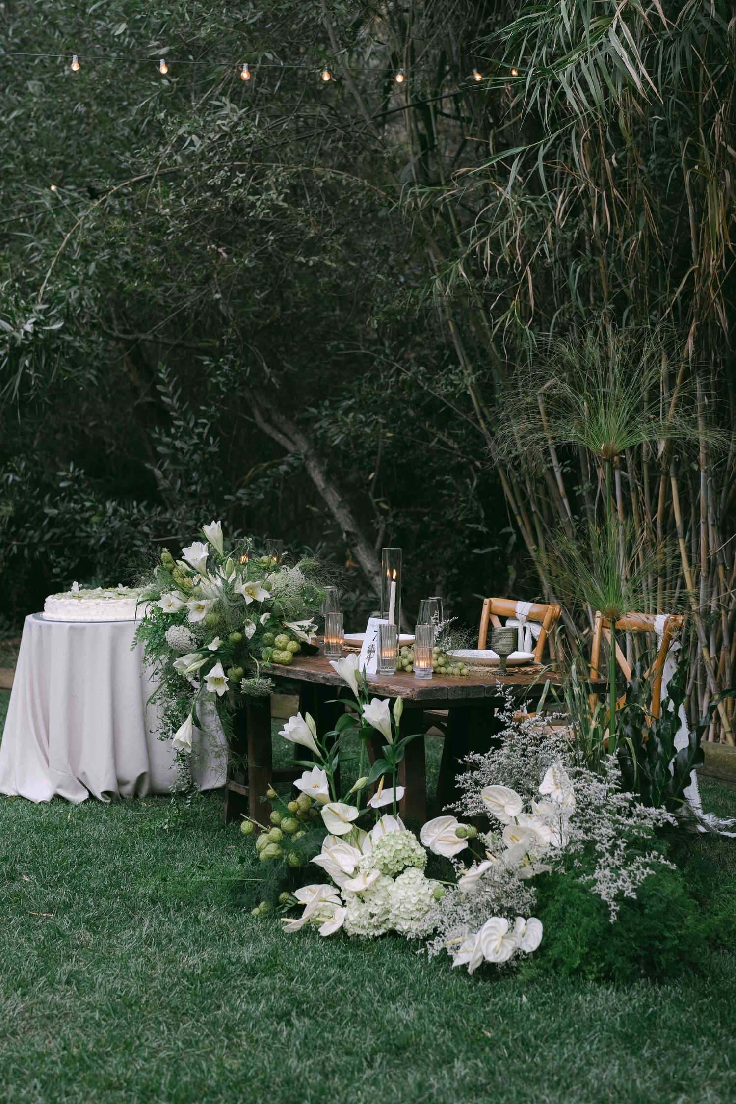 White floral arrangements and table settings nestled among lush garden greenery.