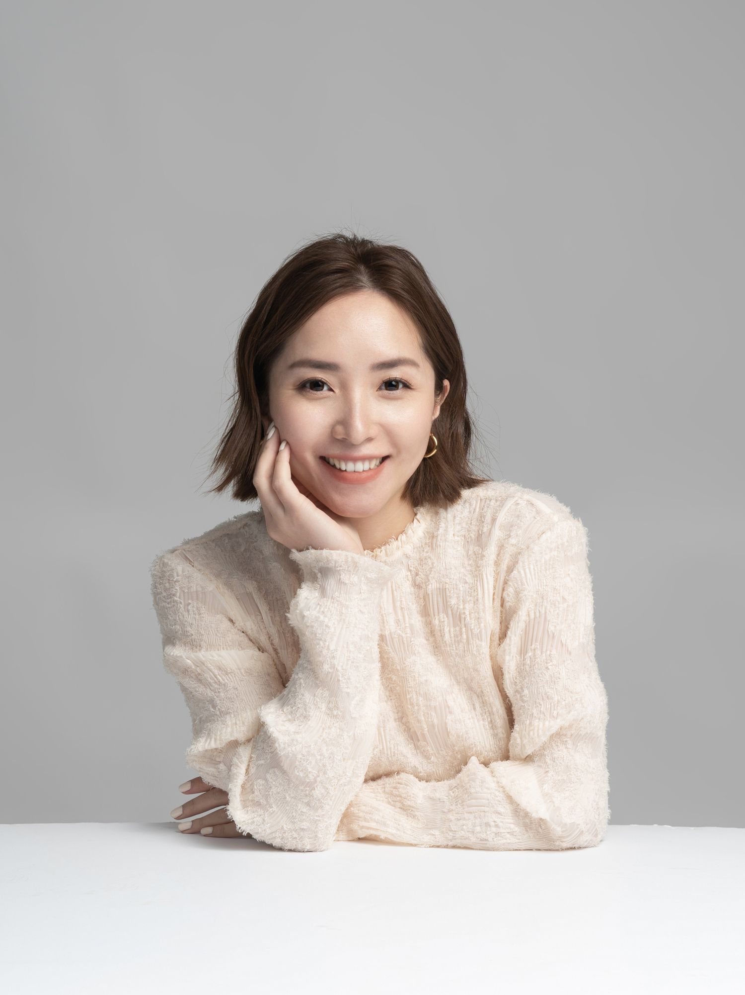 Person in cream sweater posing on white surface with relaxed expression.