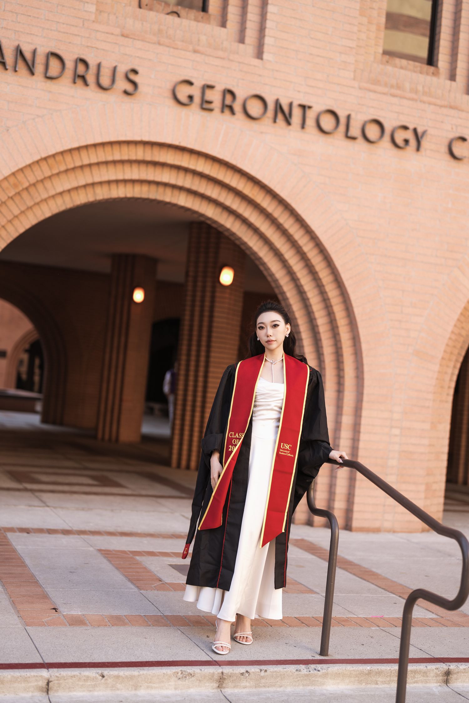 Graduate in academic regalia standing outside Andrus Gerontology Center.