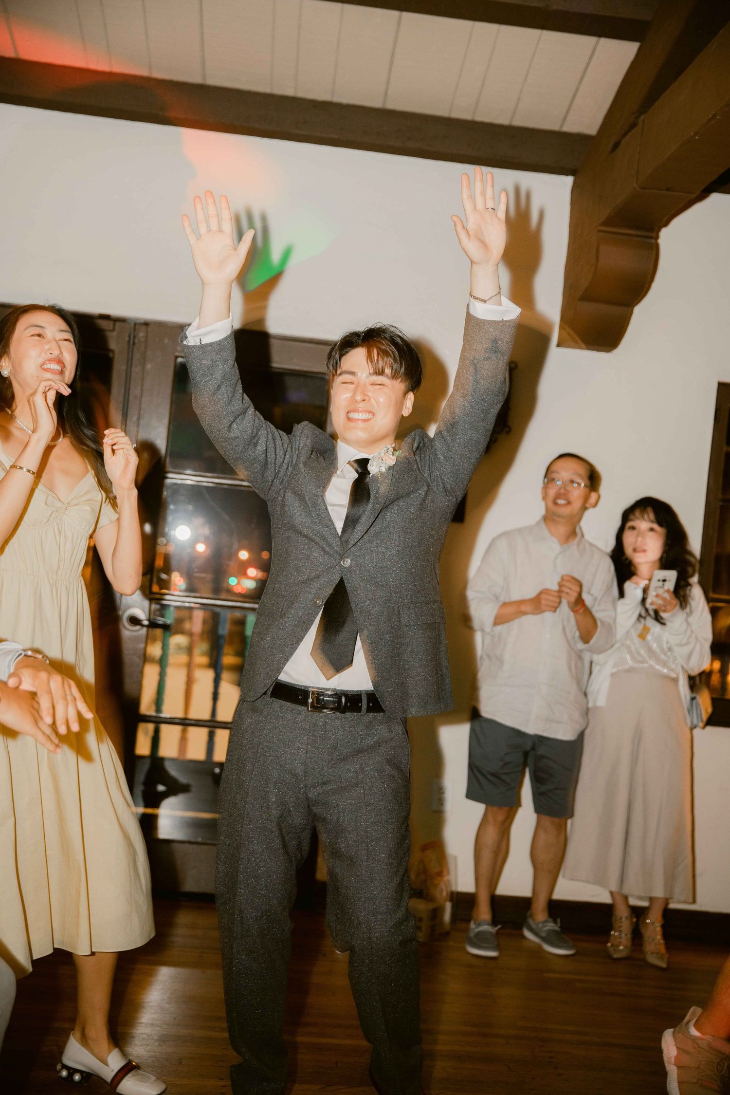 Wedding guests dancing and celebrating with raised arms on a dance floor at an indoor reception.