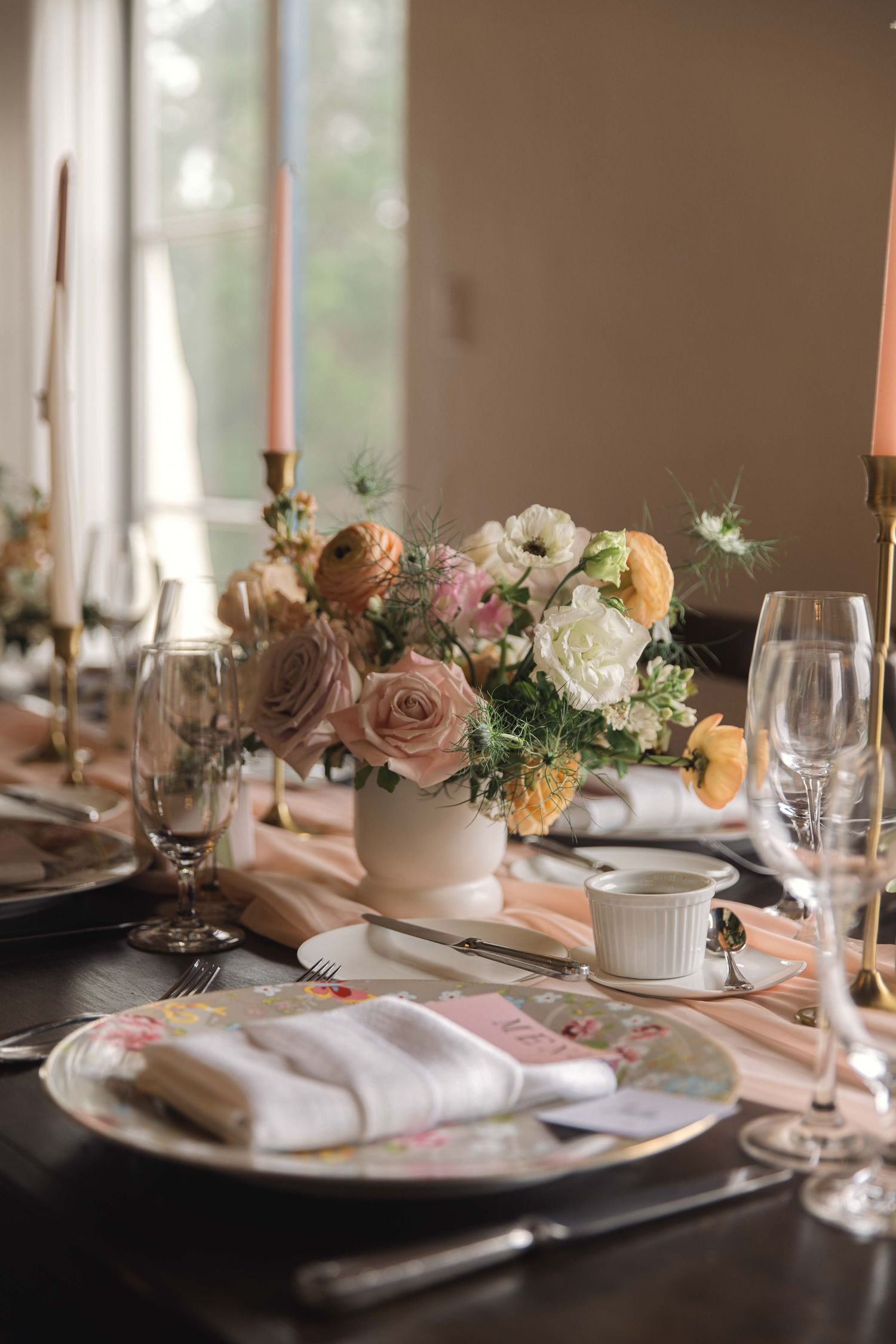 Romantic table setting with pink and peach floral centerpiece, candles, and elegant place settings.