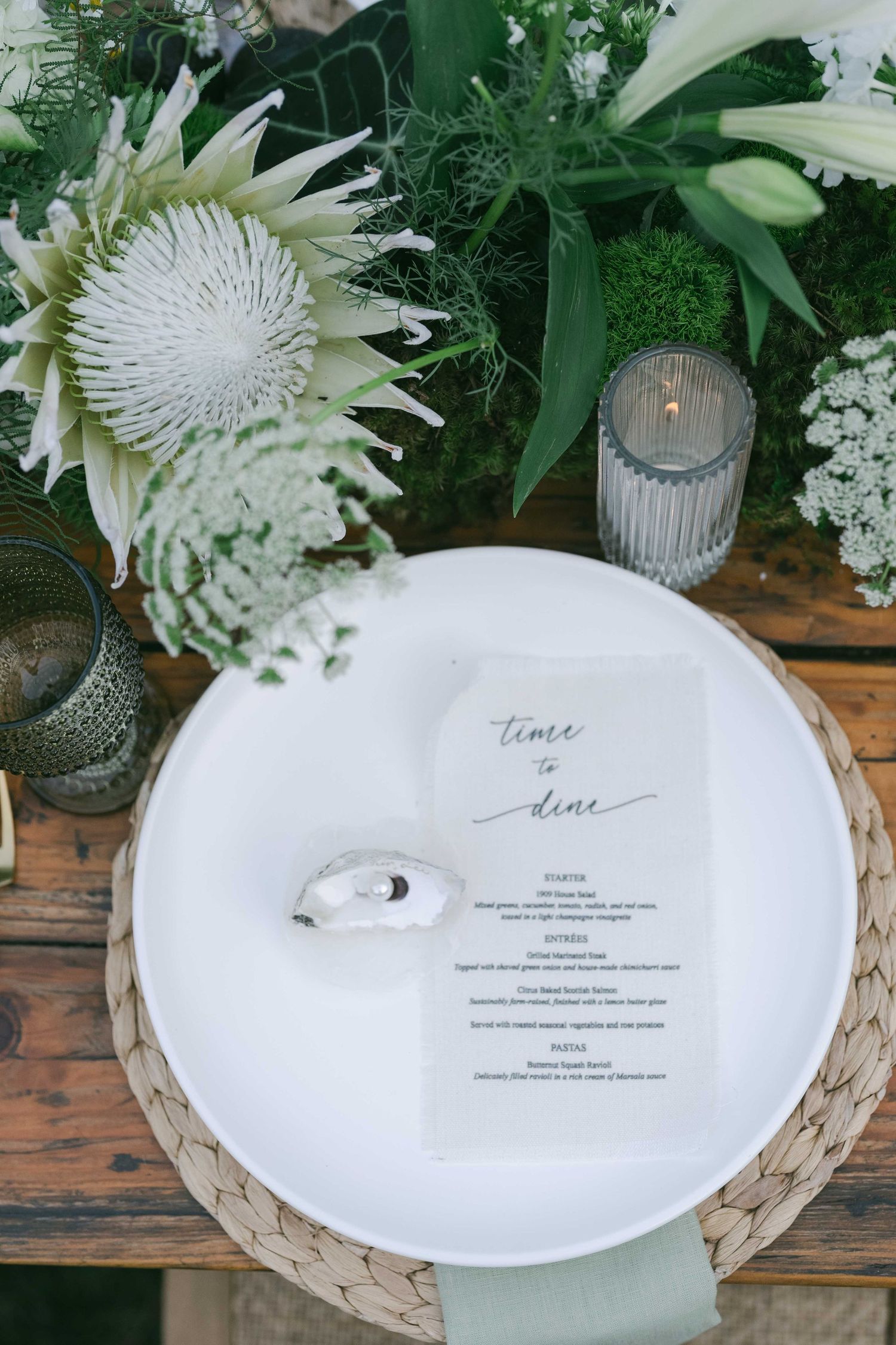 Wedding menu cards placed on white plates with floral centerpieces and glass votives.