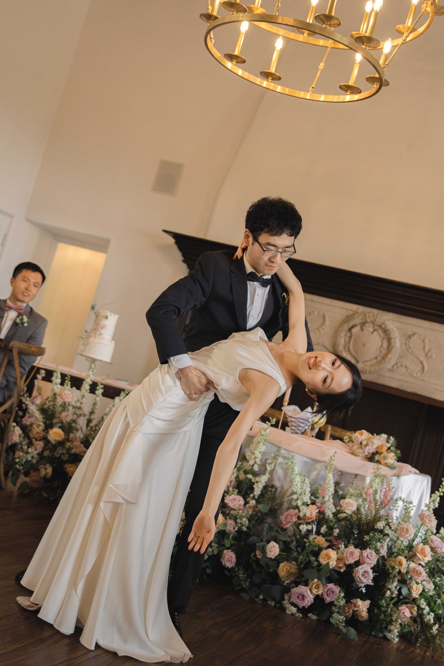 Couple performing romantic dance dip move near floral arrangements at reception.
