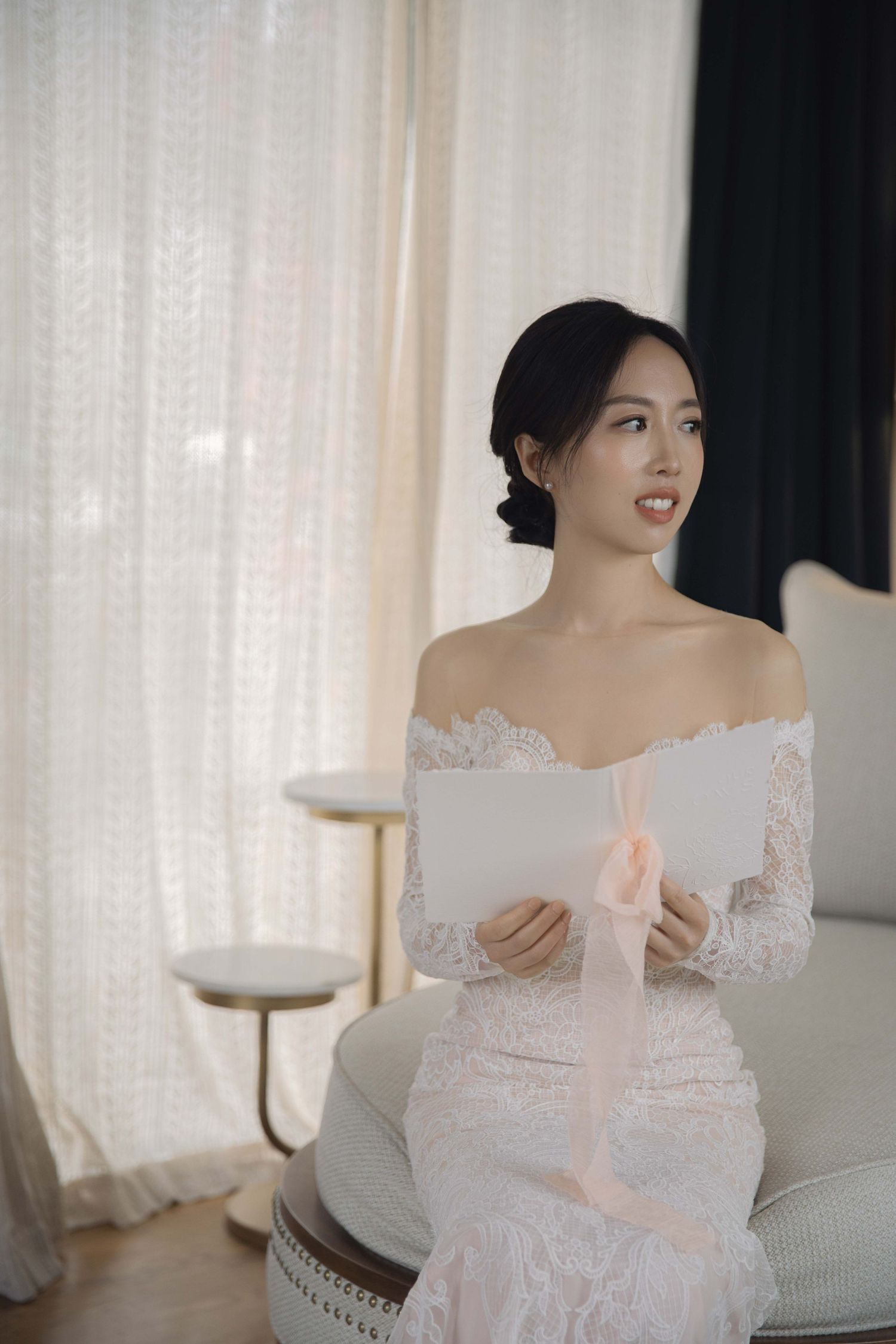 Person wearing delicate white lace dress poses near sheer curtains in an elegant setting.