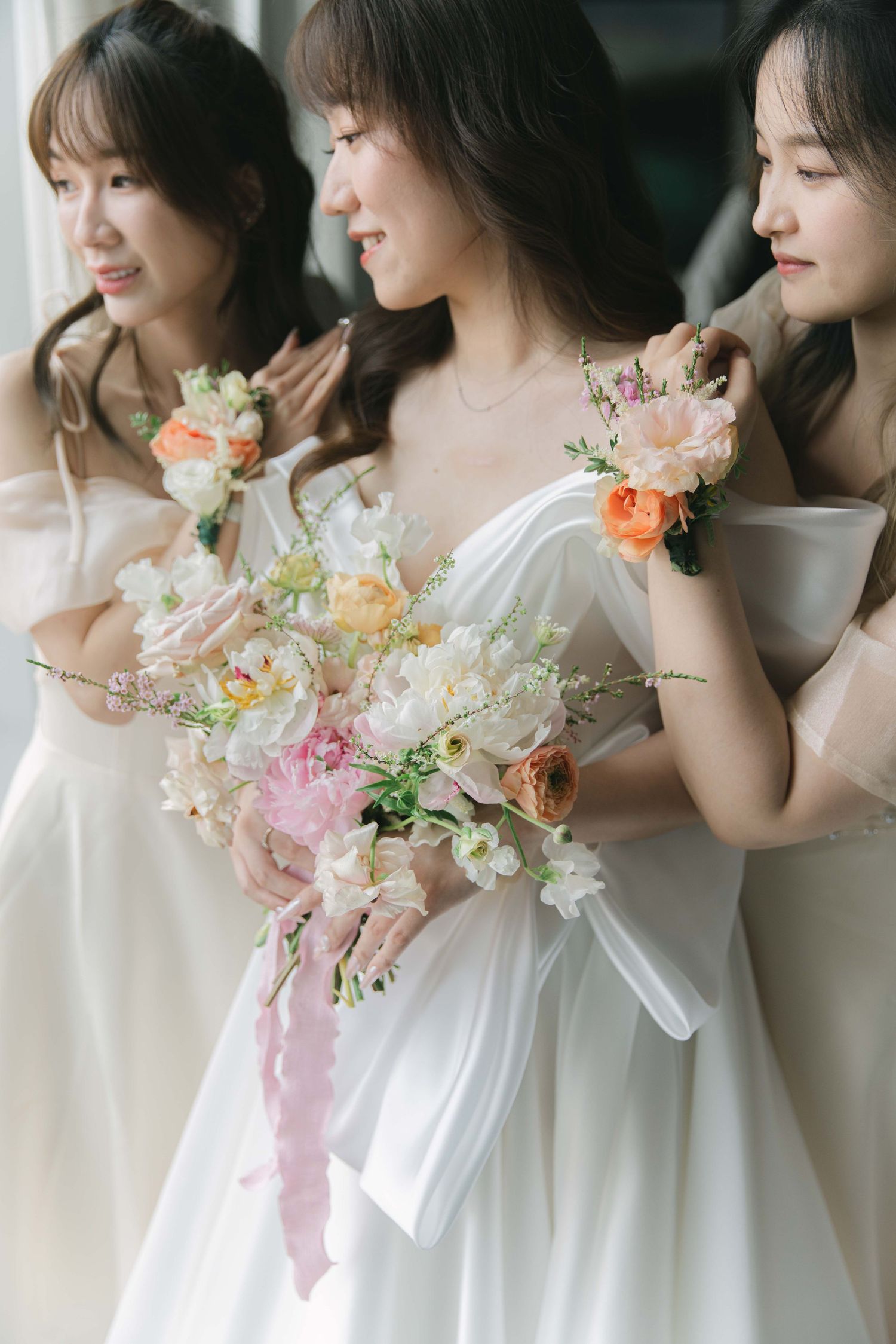 Row of bridesmaids in white dresses holding elegant floral bouquets with peach and pink blooms.