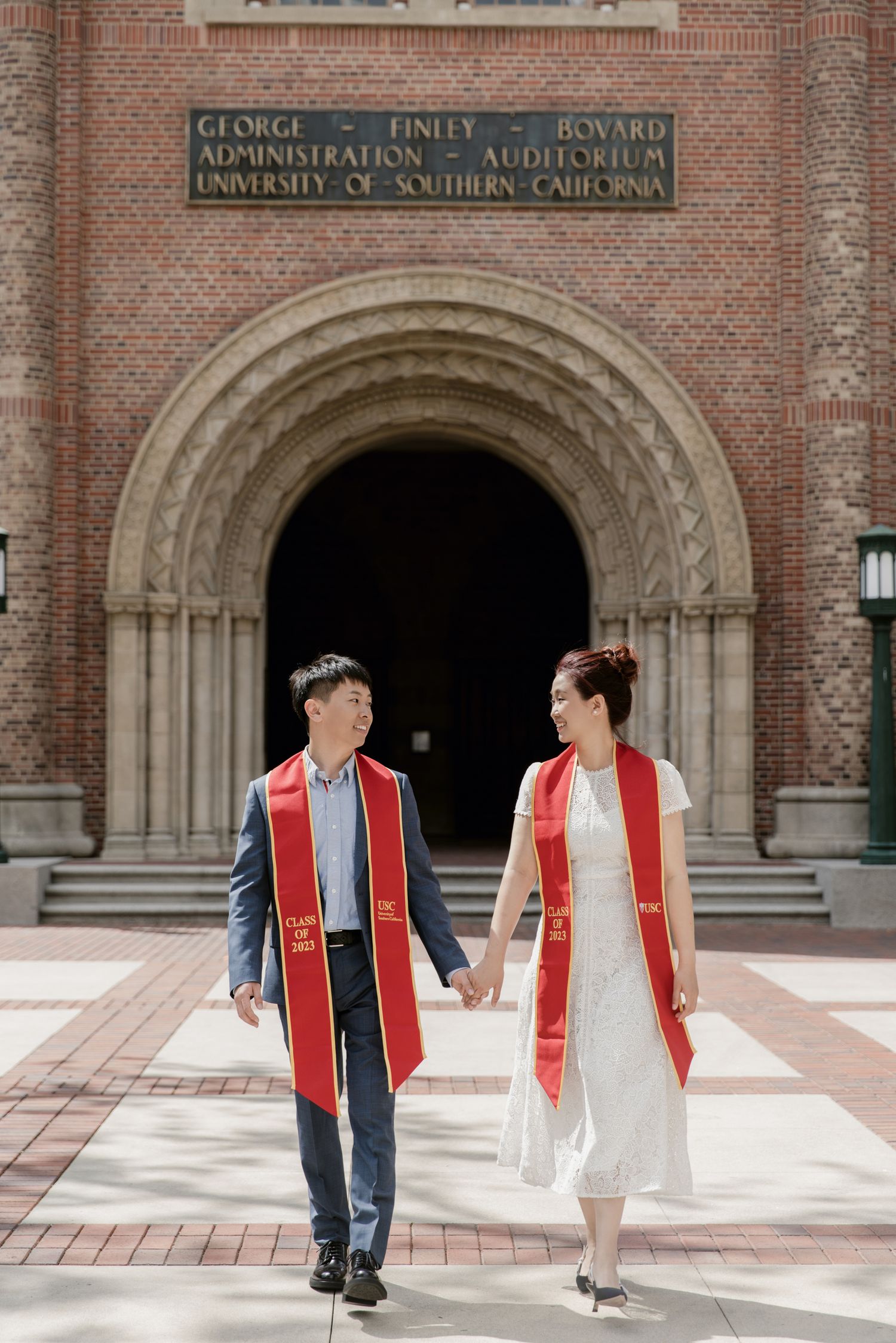 Graduates in academic regalia pose outside Bovard Administration building at USC.