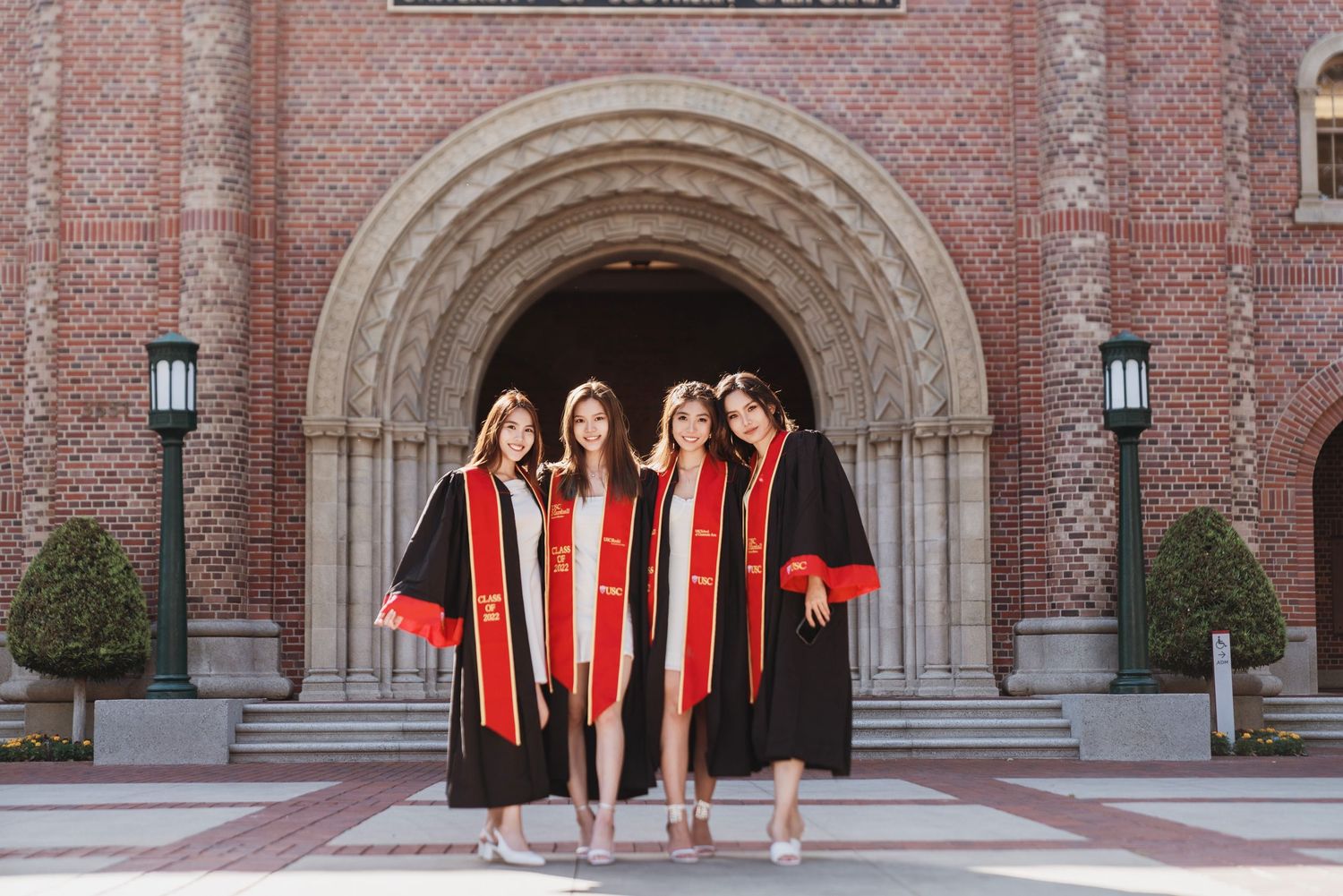 Graduates in red stoles pose together in front of historic brick university building entrance.