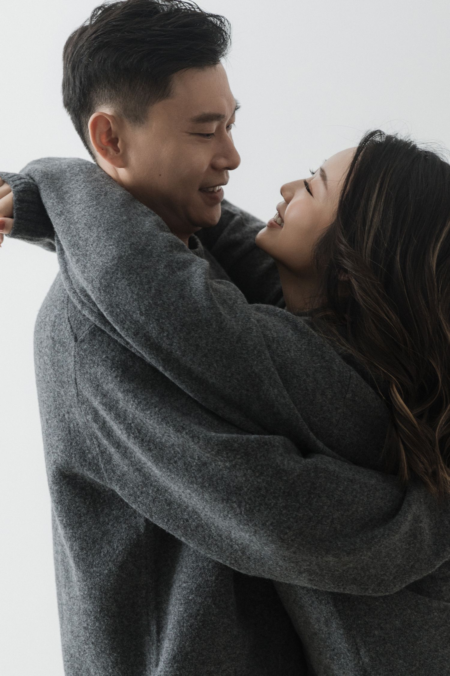 A couple wearing matching gray sweaters share an intimate moment against a light background.