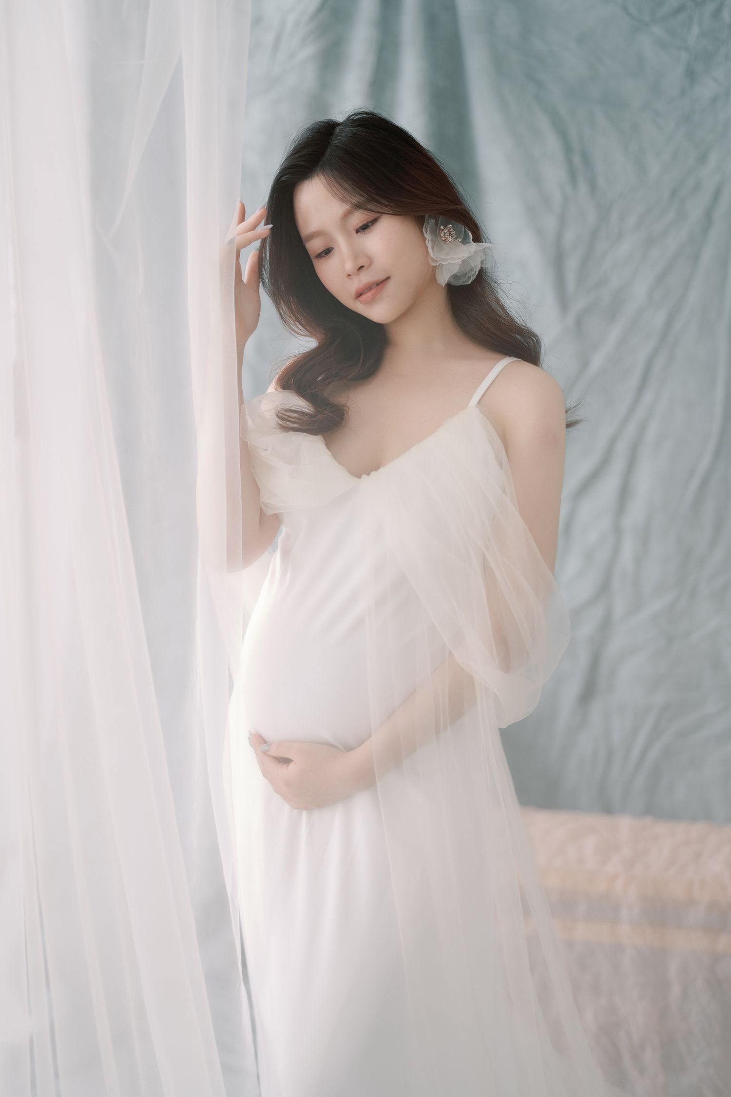 Dreamy maternity photoshoot with flowing white fabric and soft lighting.