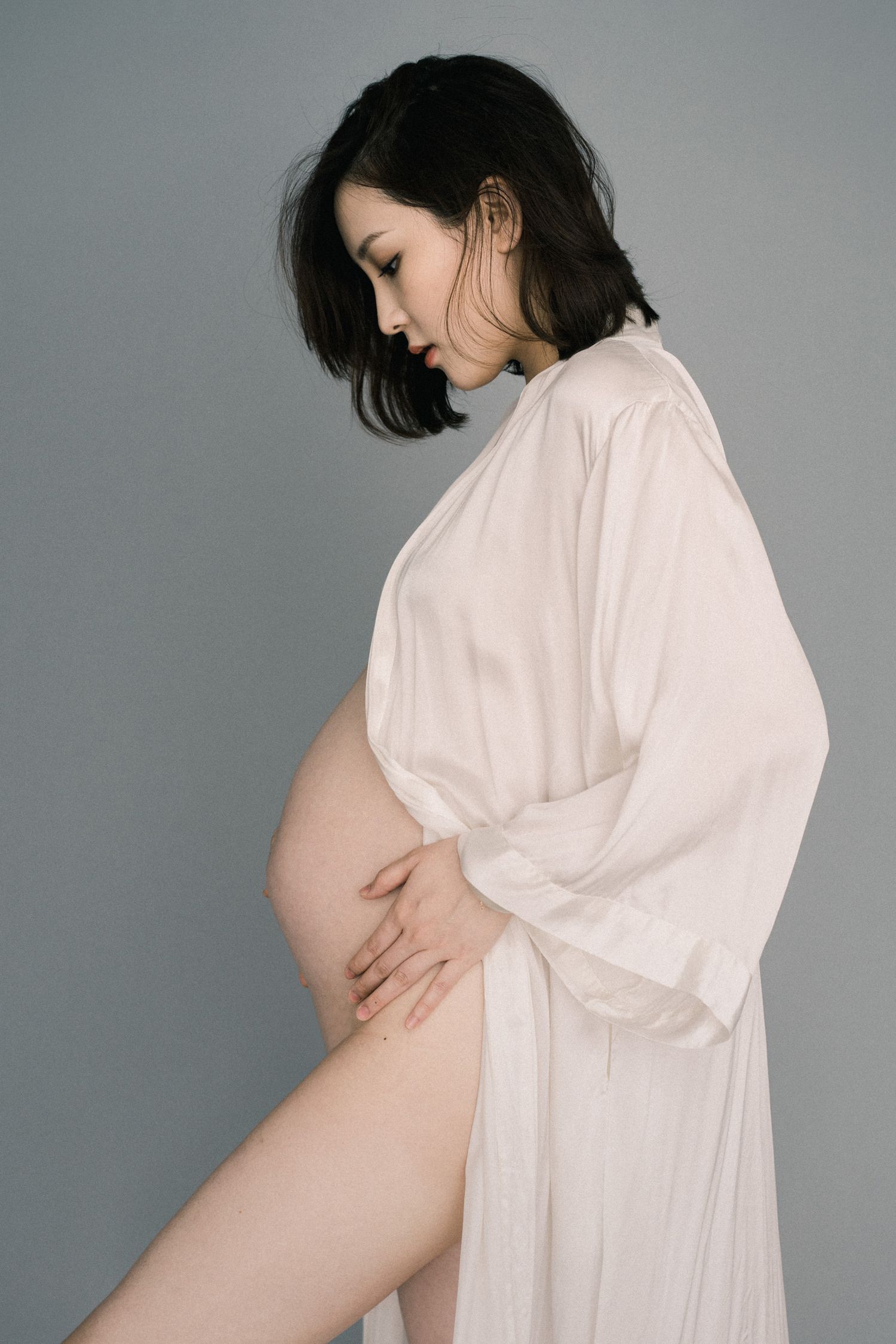 Minimalist maternity portraits in white dress against grey background.