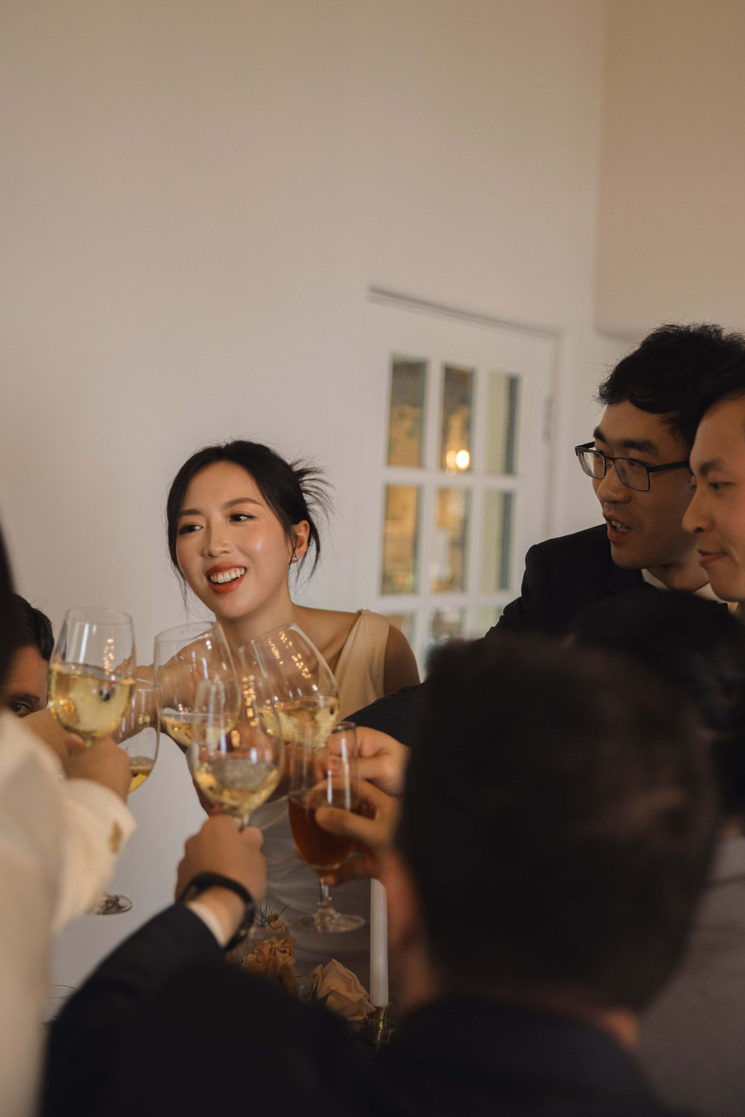 Wedding guests clink glasses in a celebratory toast at an indoor reception.