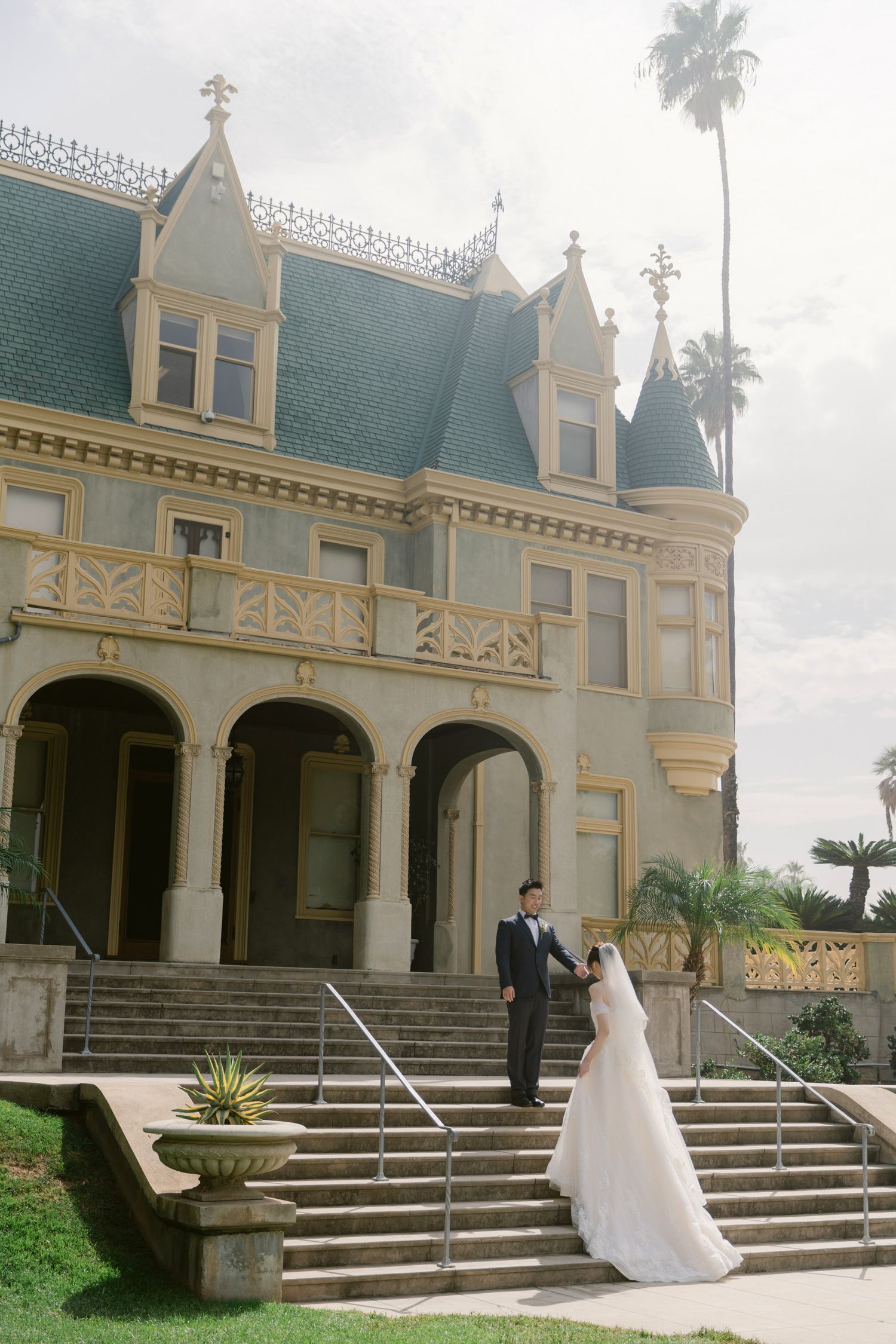 Grand Victorian-style mansion with sweeping steps and elegant architecture serves as a wedding venue.