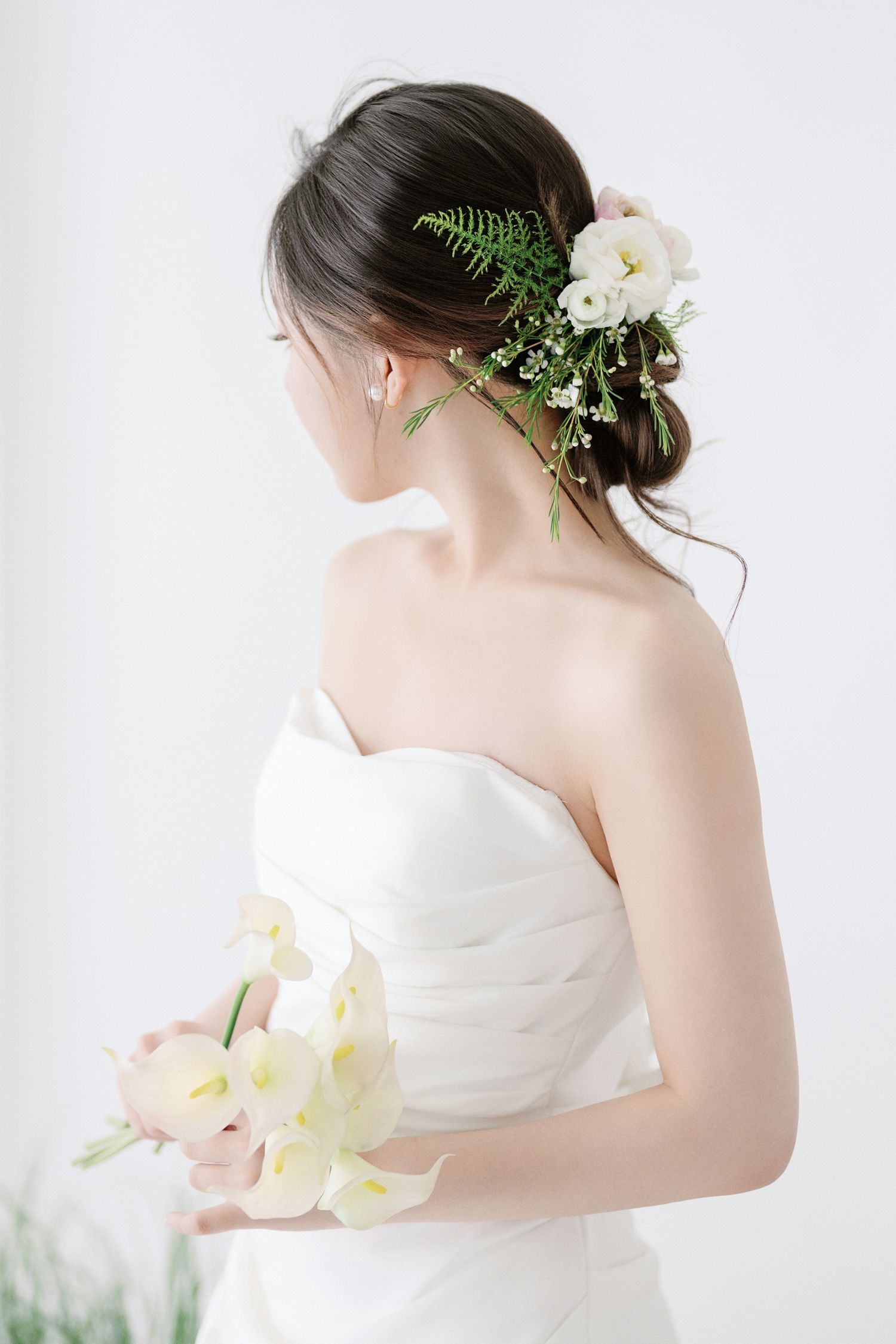 Elegant bridal portrait featuring a white strapless dress adorned with delicate fern and floral hair accessories.