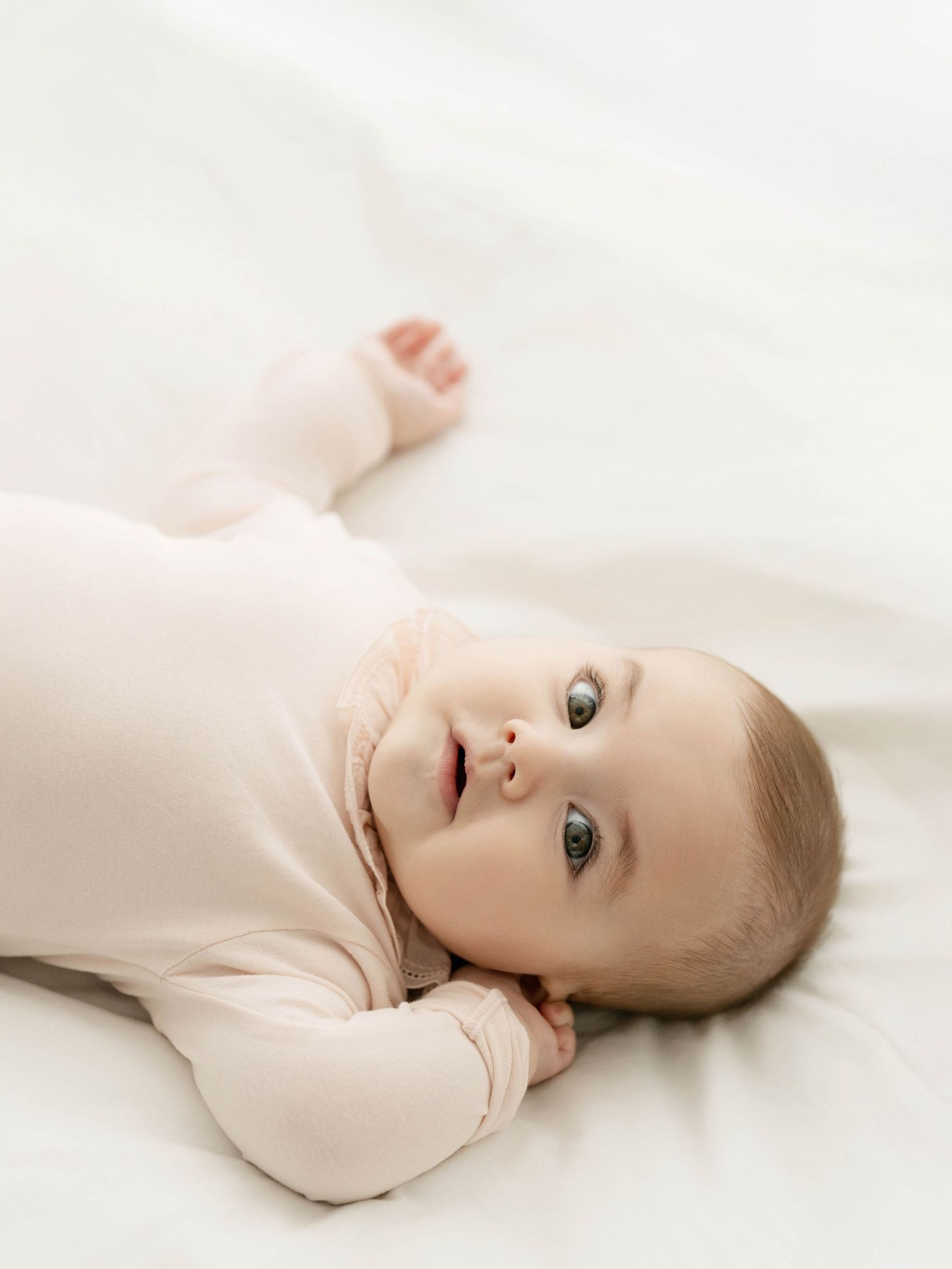 Baby in cream colored outfit lying on white background during studio photoshoot.