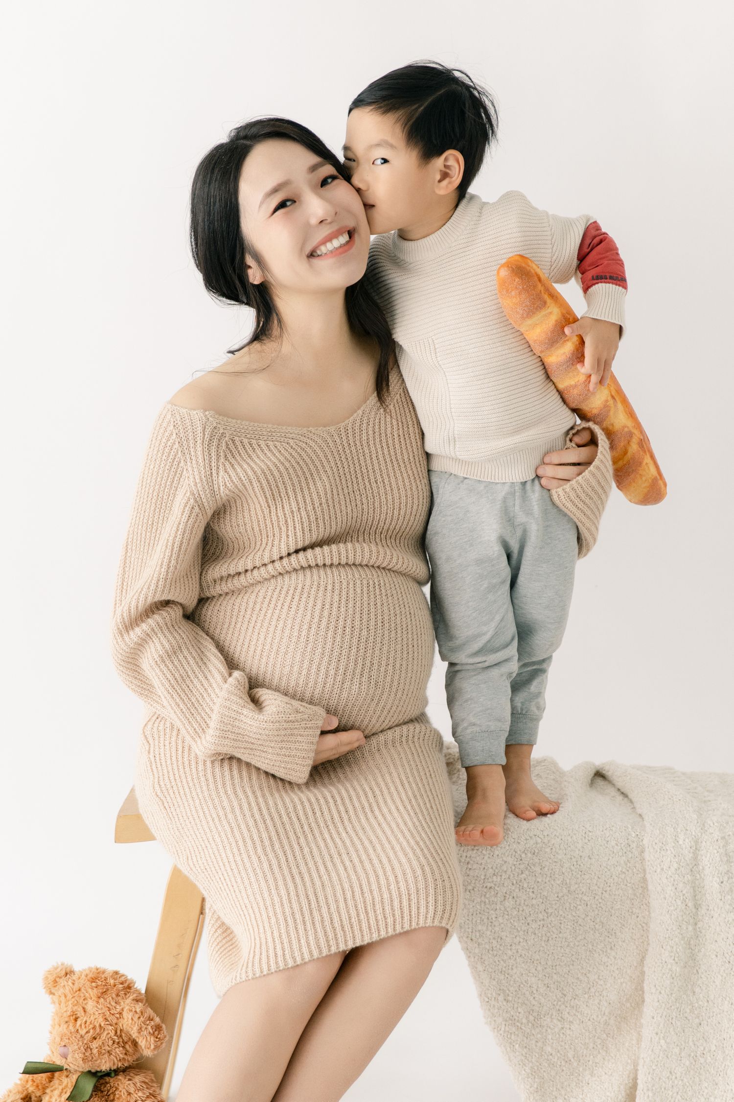 Sweet maternity moments with teddy bear props against white backdrop.