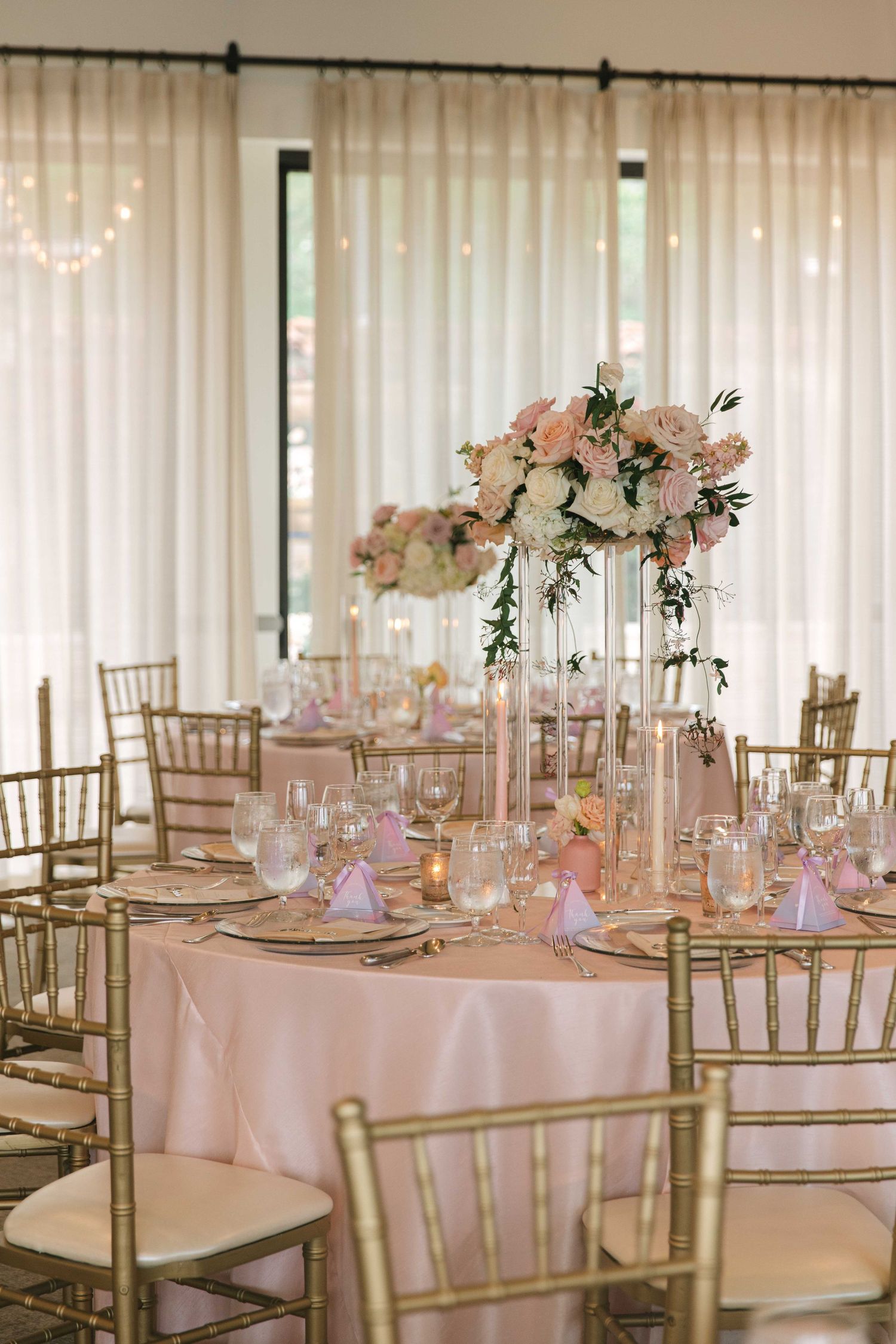 Elegant wedding reception tables with pink floral centerpieces and gold chiavari chairs.