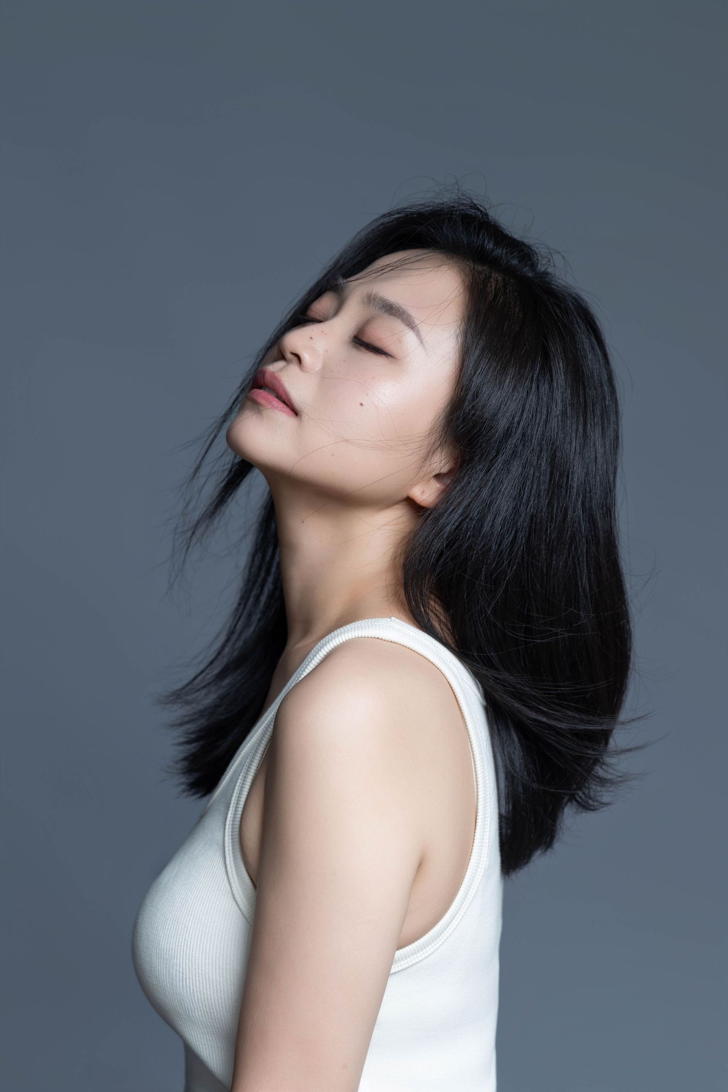 Artistic profile shot with dynamic hair movement against grey backdrop.