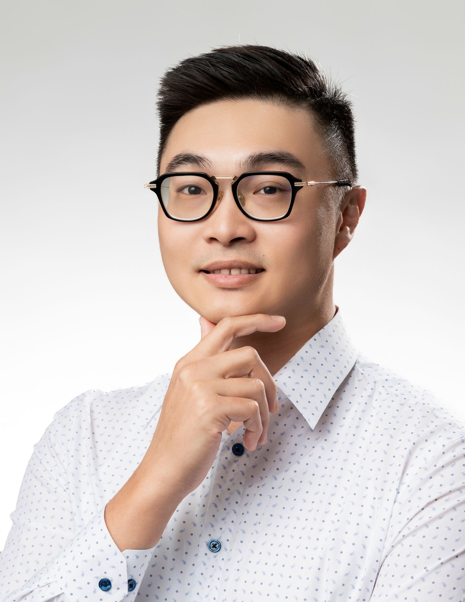 Professional headshot of person in glasses and white polka dot shirt against light background.