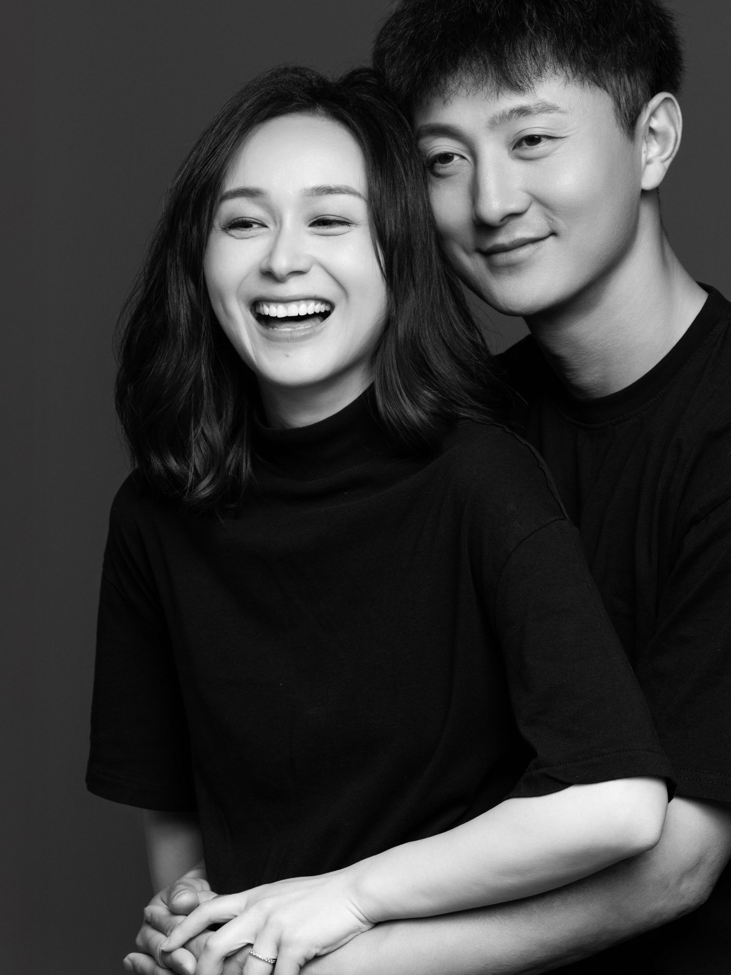Black and white portrait of a couple in matching dark outfits sharing an intimate moment.
