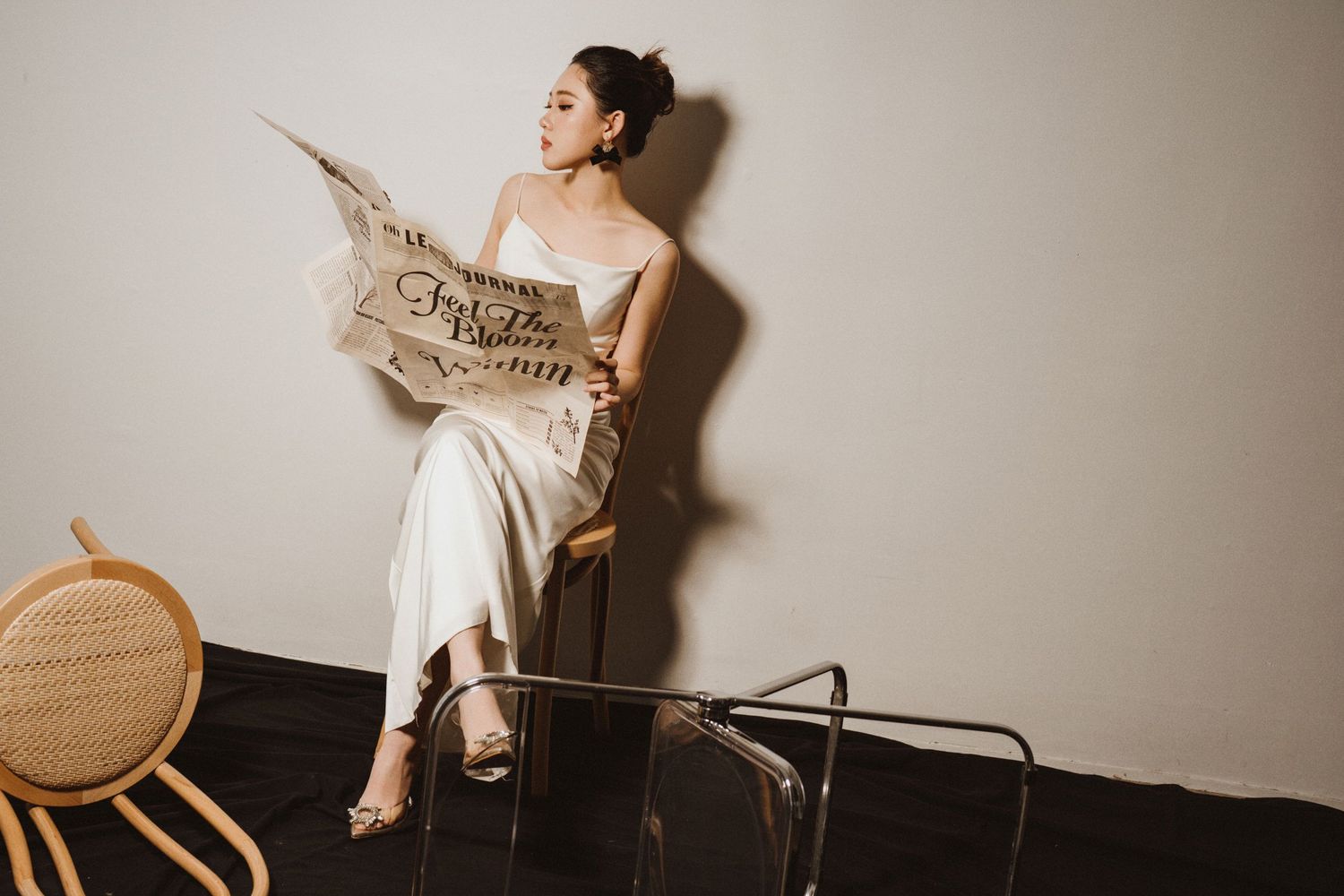 Artistic fashion photography featuring white dress and wooden chair against neutral wall.