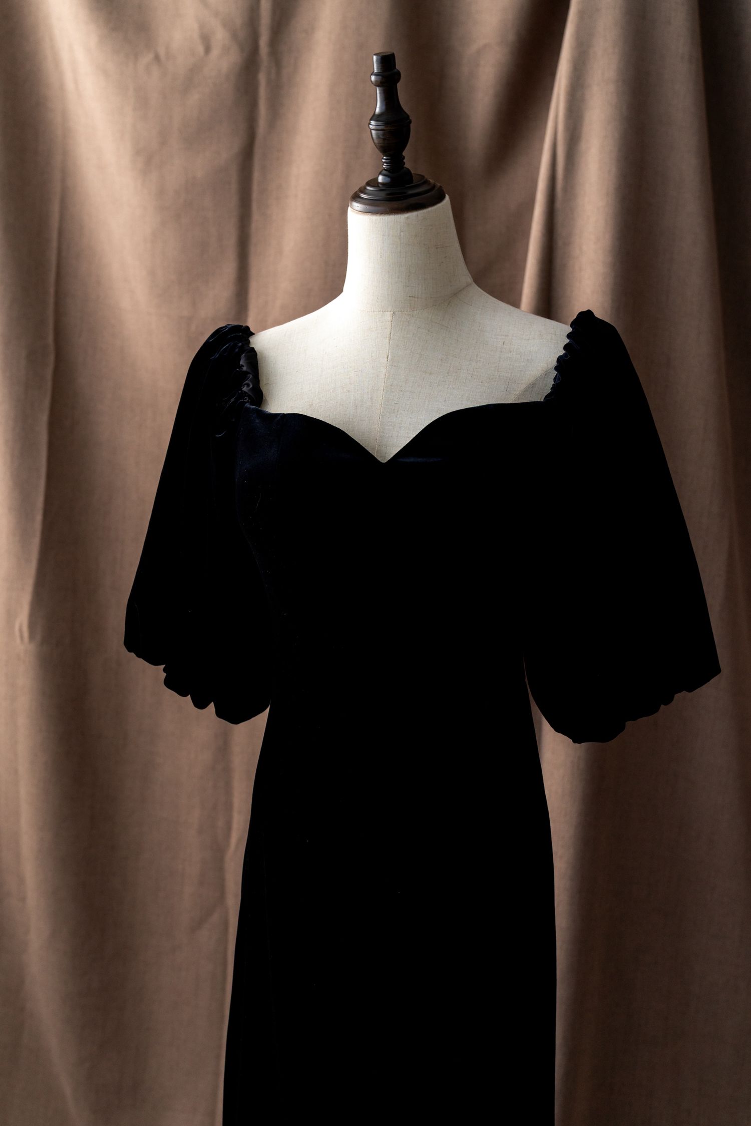 Black formal dress with puff sleeves displayed on mannequin against brown backdrop.