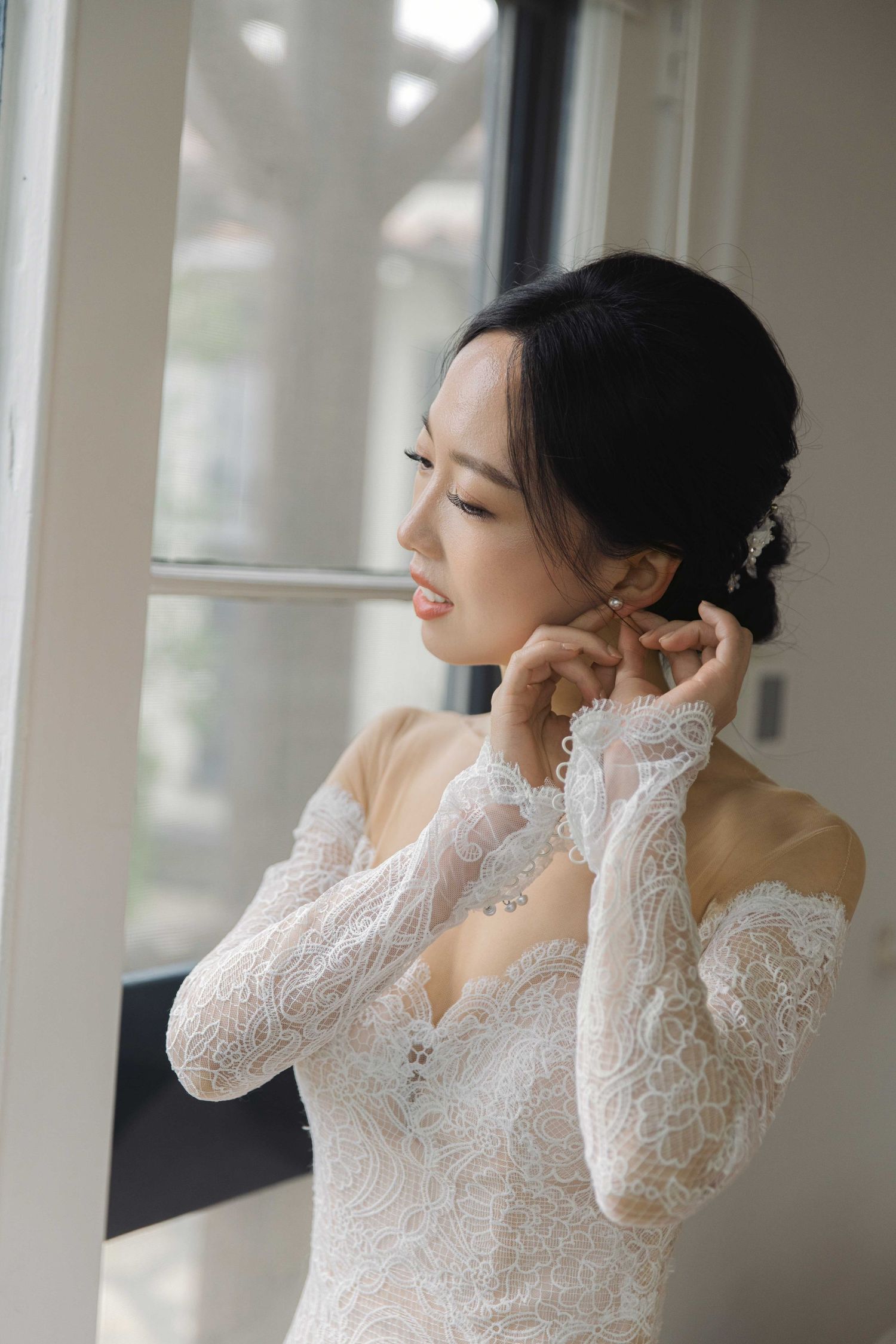 A delicate white lace wedding dress is showcased in a bright interior setting with natural lighting.