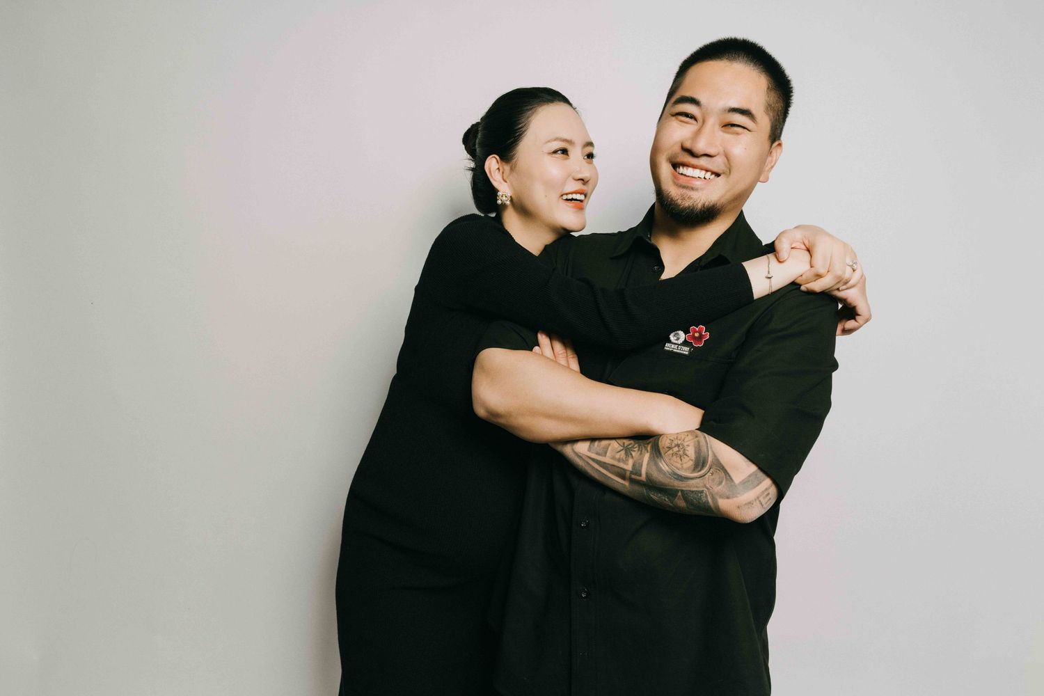 Playful studio portrait of couple in matching black outfits against white background.