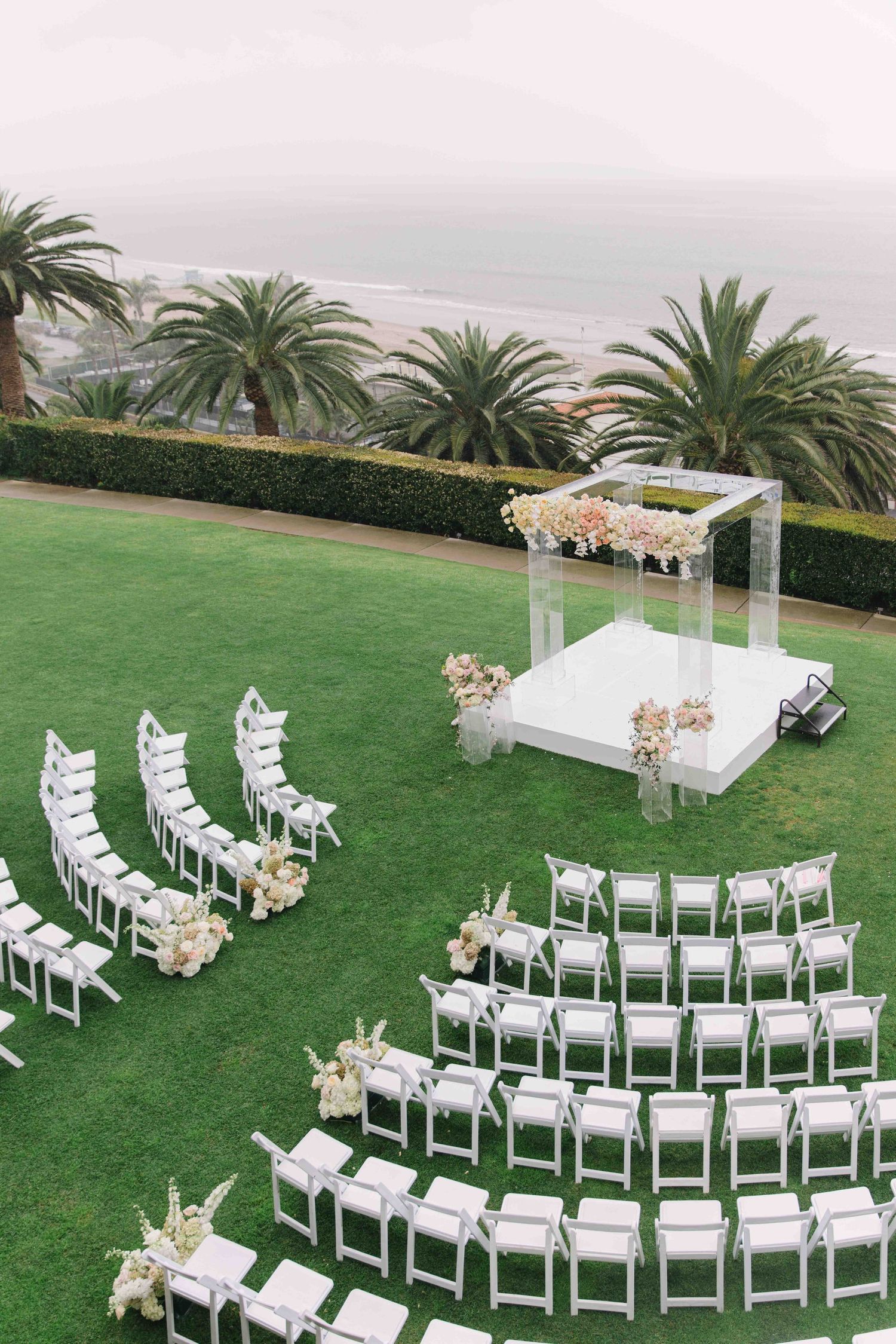 Outdoor wedding ceremony setup with white chairs arranged in semi-circles on manicured lawn.