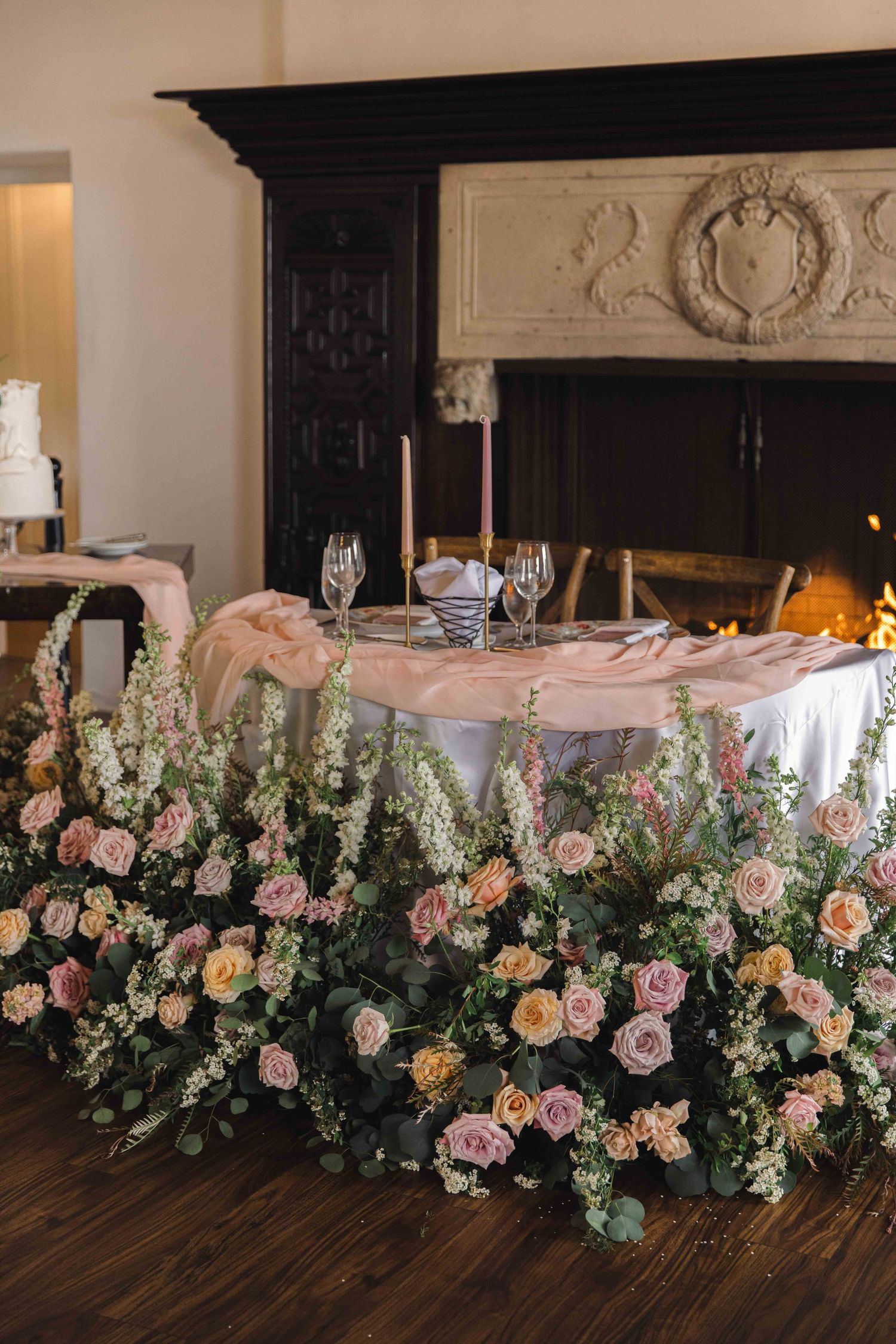 Luxurious floral arrangement with pink and peach roses cascading from an elegant table near a fireplace.