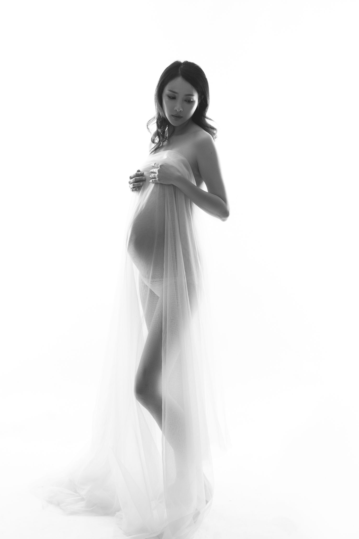 High-key maternity portraits in white flowing fabric creating dreamy silhouettes.