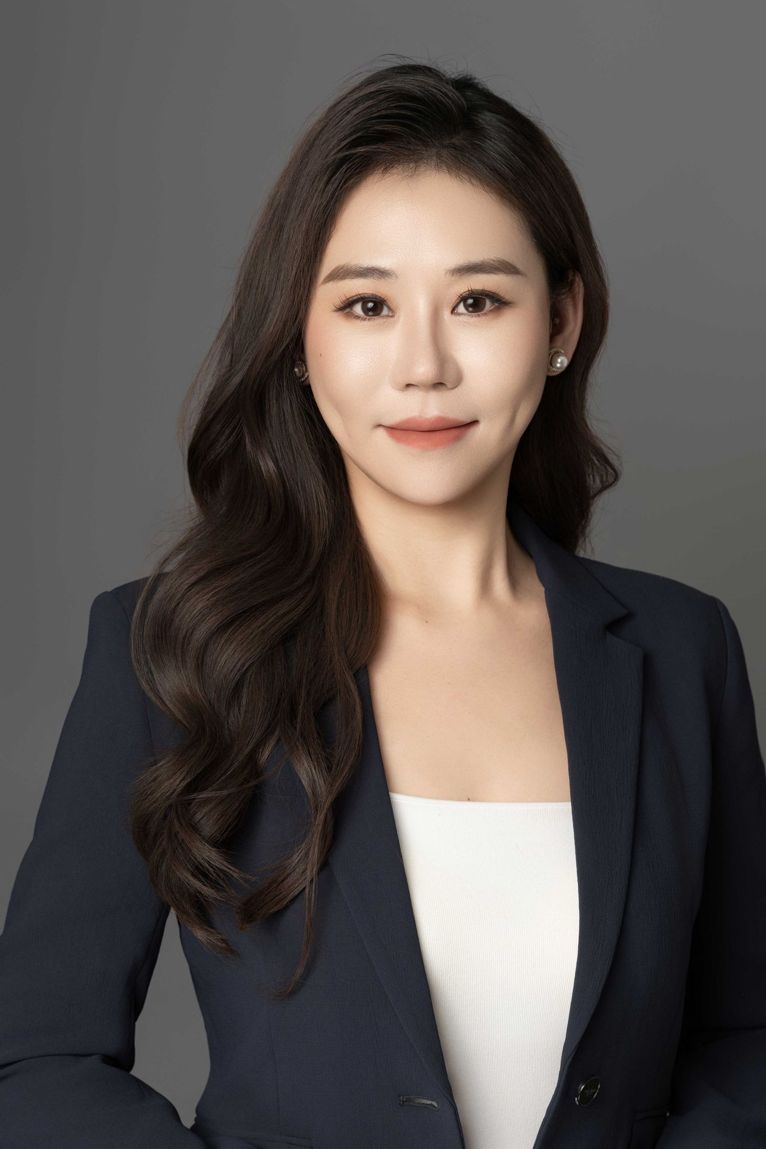 Professional headshot of person in navy blazer and white top against gray background.