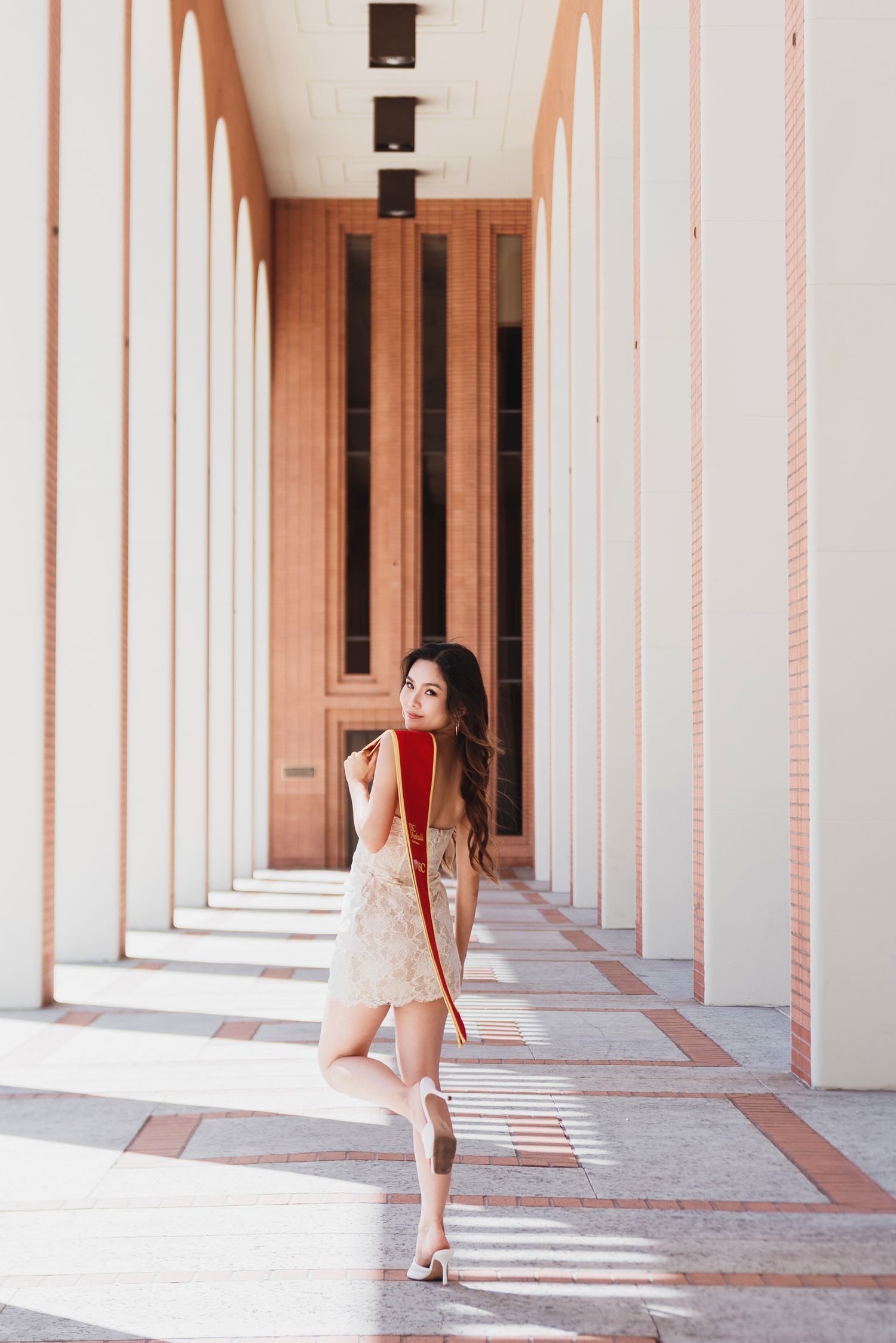 Graduate in white dress poses in USC's architectural colonnade.