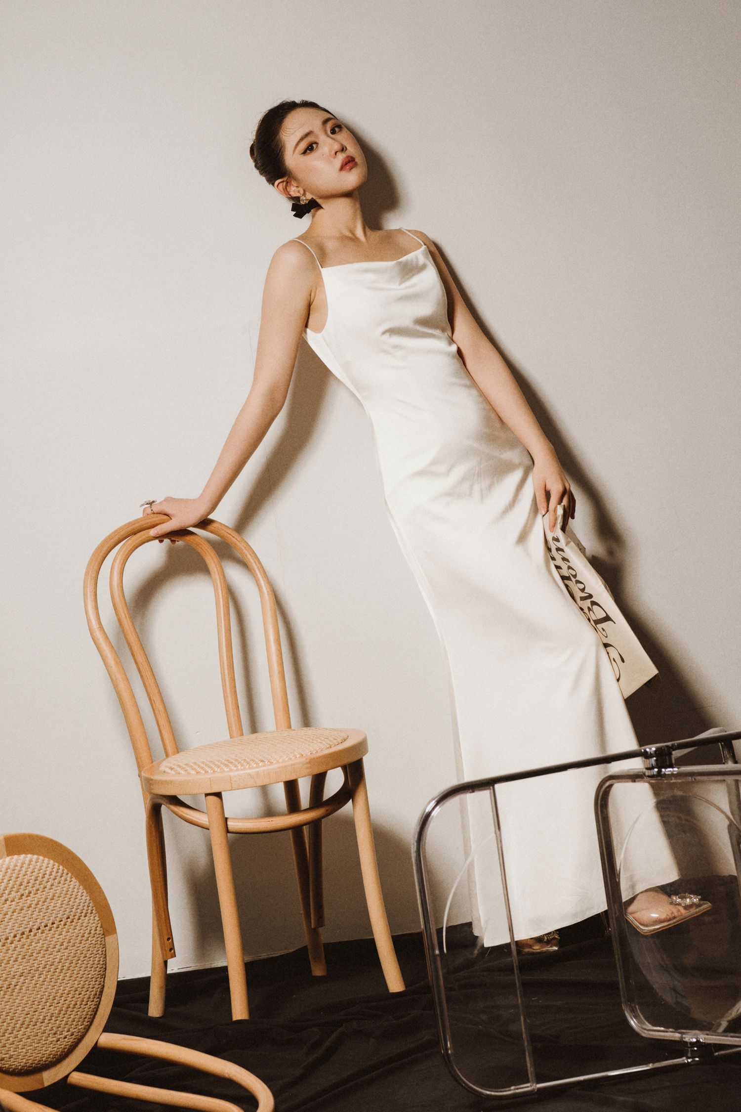 Minimalist fashion photograph with wooden chairs and white dress in studio.