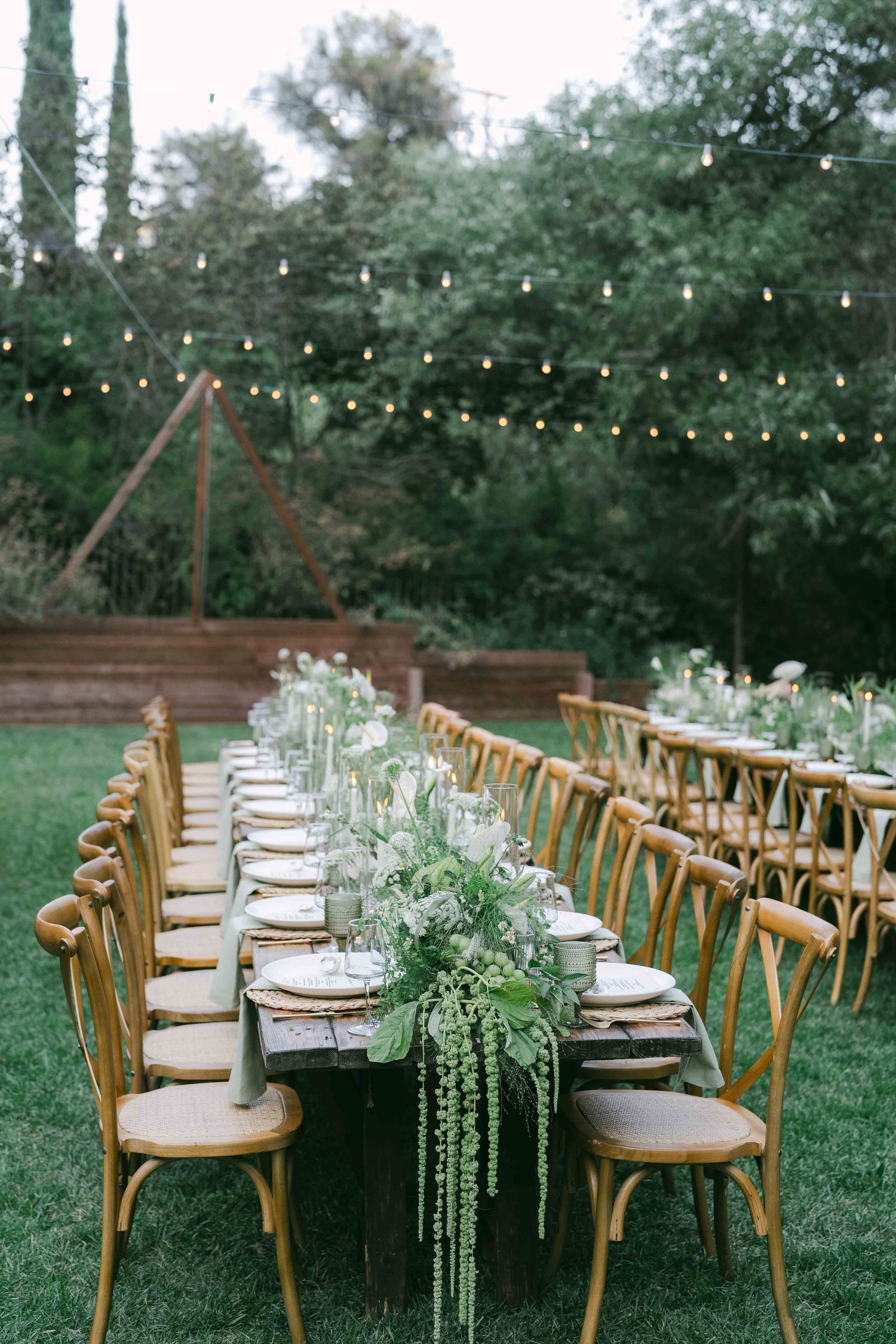 Outdoor reception setup with wooden chairs and string lights creating an enchanting garden atmosphere.