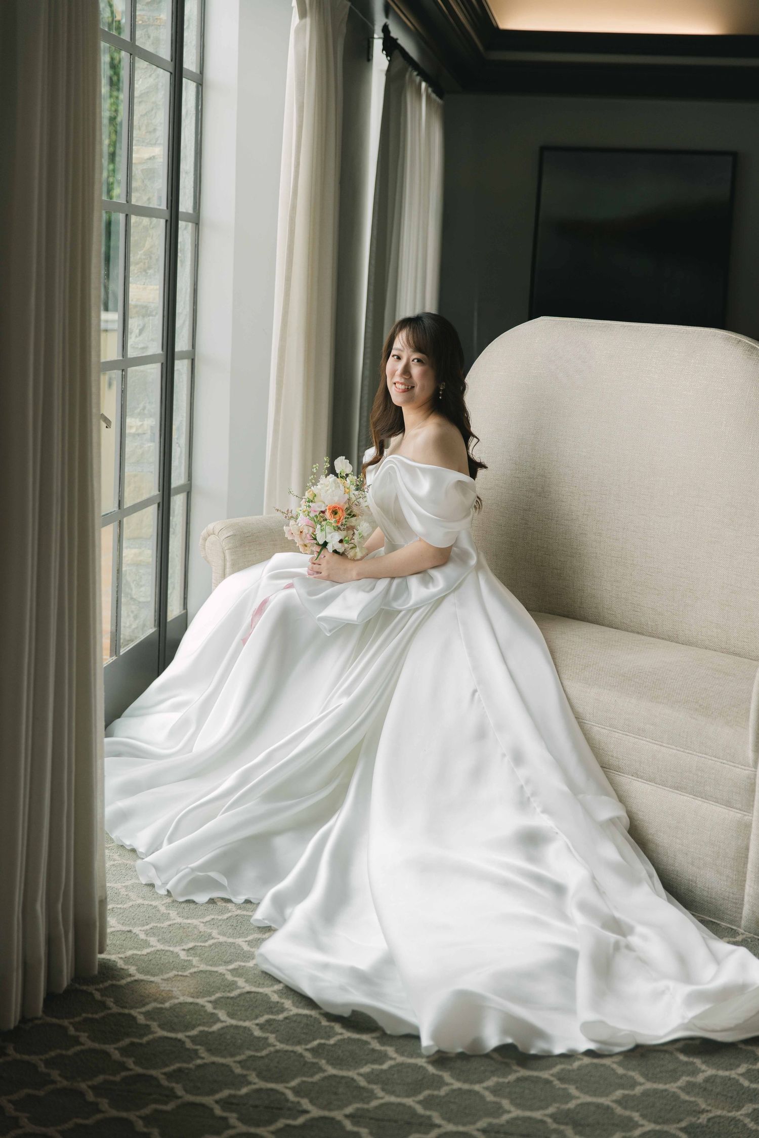 Elegant white wedding dress flowing across a patterned floor near large windows.