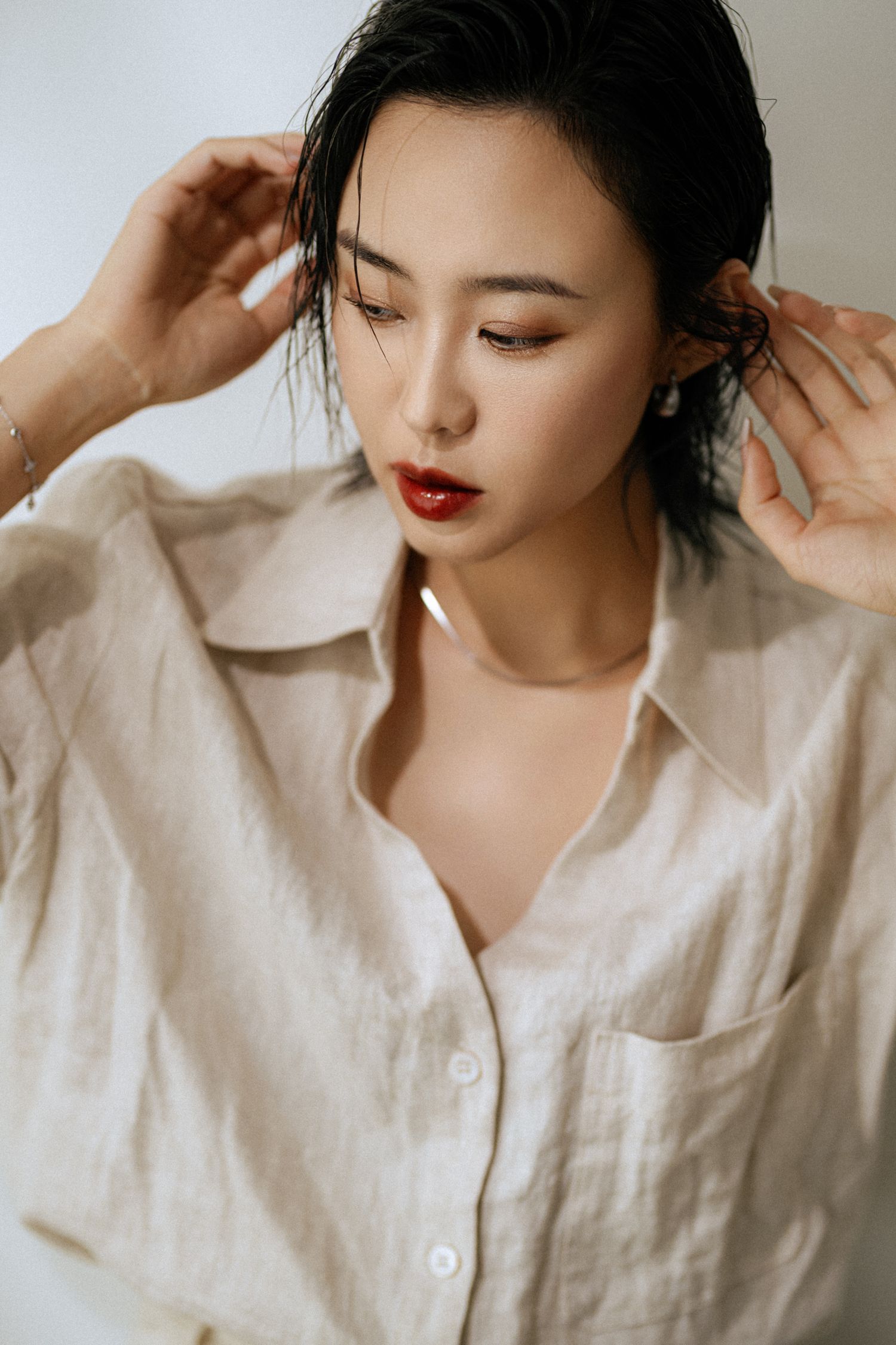 Woman in white linen shirt poses artistically while adjusting her collar.