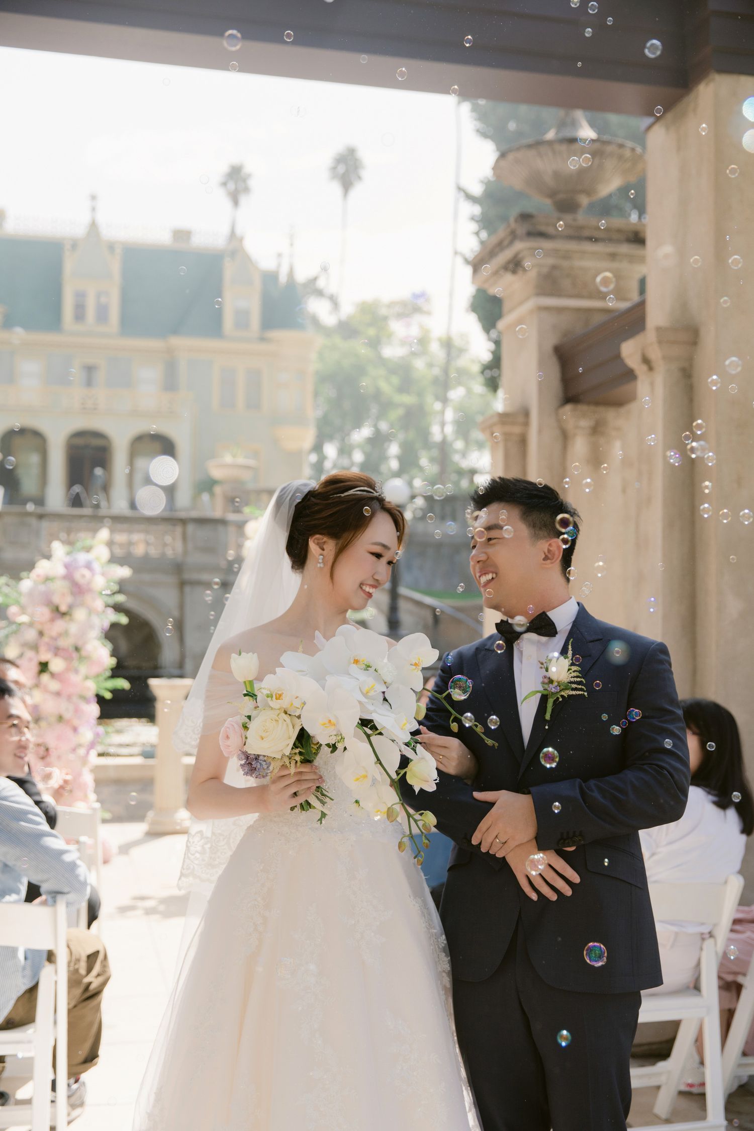 Joyful wedding moment with bubbles floating through the air at an outdoor venue.