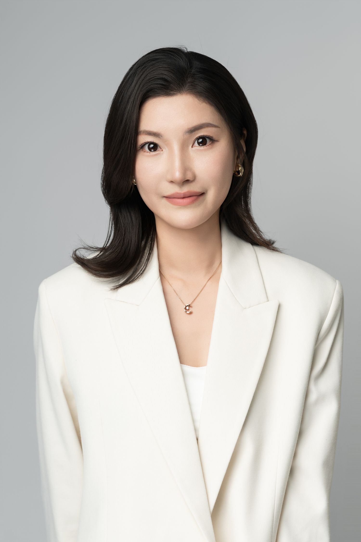 Professional headshot of a person in a white blazer against a neutral gray background.