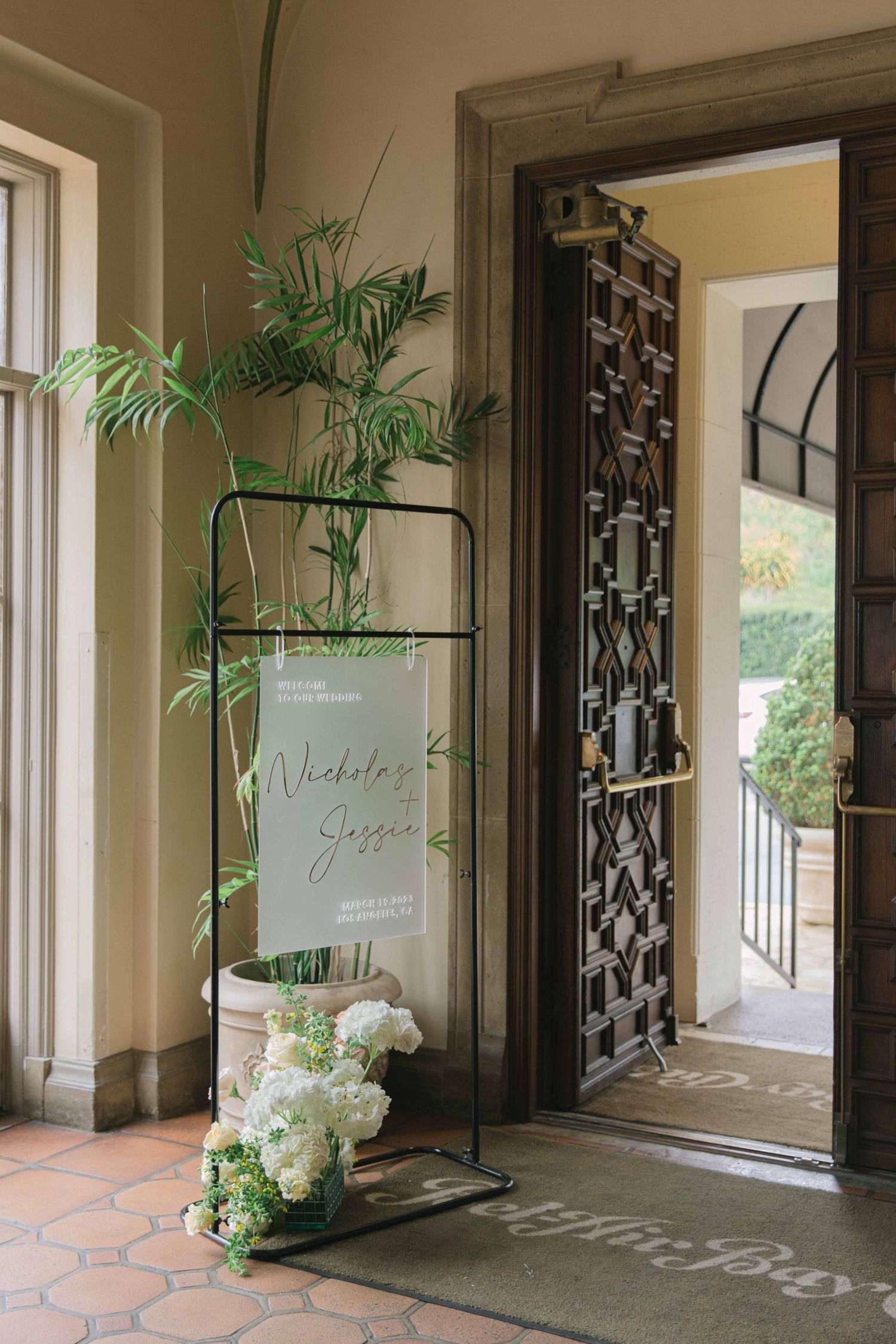 Modern wedding welcome sign display with white hydrangeas and greenery in an elegant hallway.