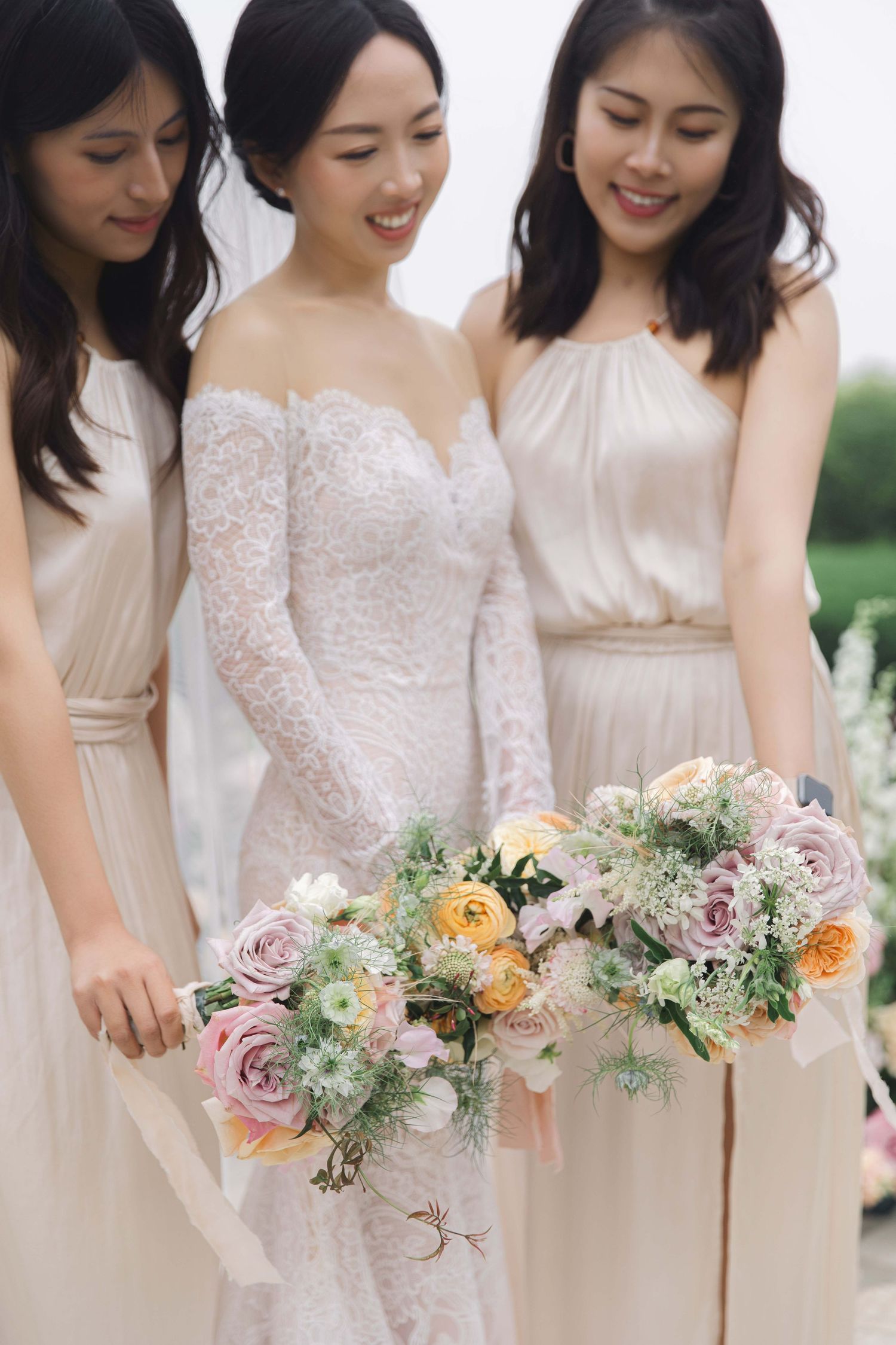 Bridesmaids in cream dresses hold delicate pastel floral bouquets.