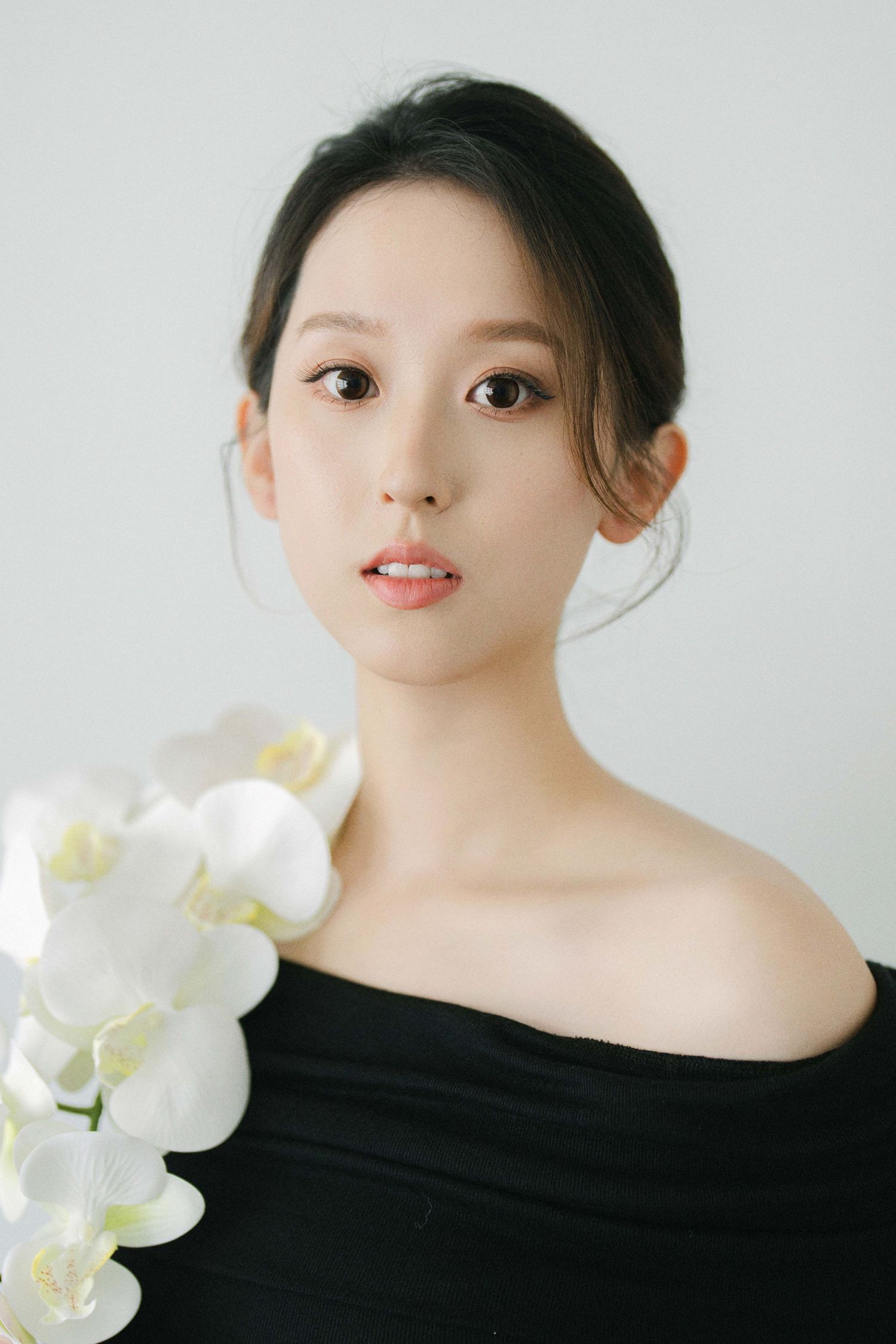 Portrait with white orchids against white background featuring elegant black off-shoulder styling.
