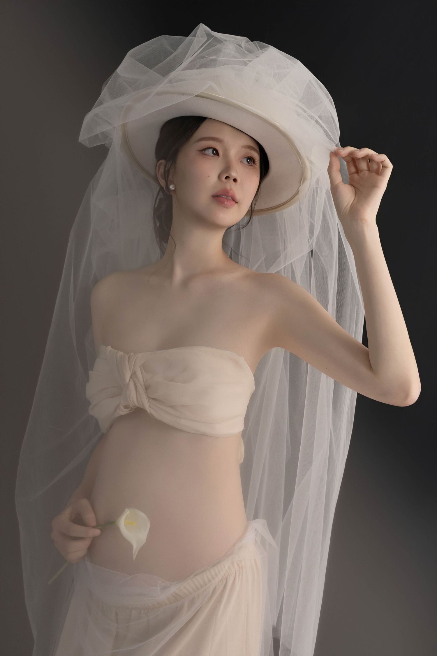 Dramatic maternity portrait with flowing veil and gentle lighting against dark background.