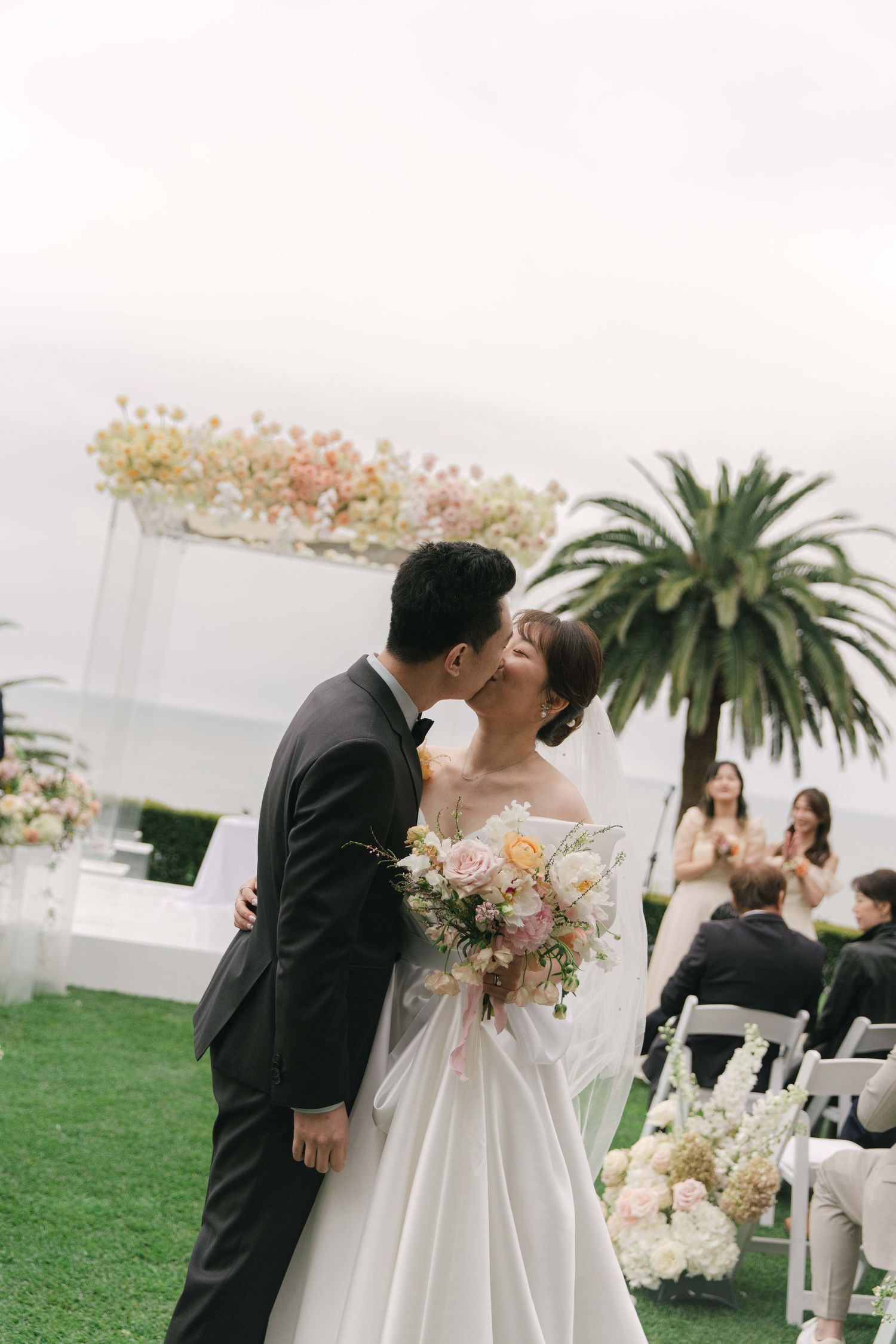 An outdoor wedding ceremony with white chairs and tropical palm trees in the background.