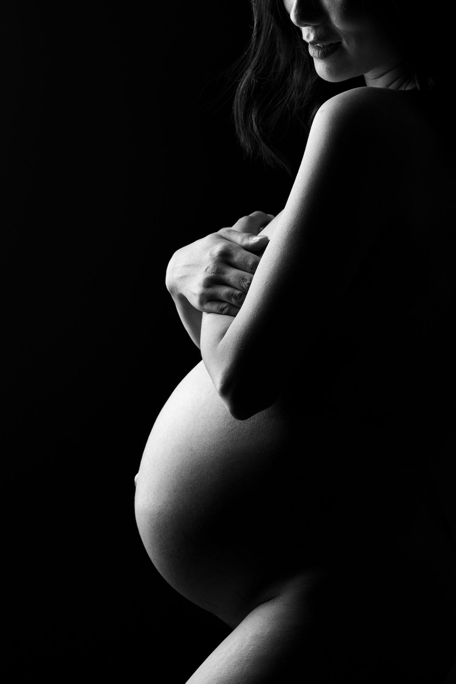 Artistic black and white nude silhouette study showing feminine curves and shadows against dark background.