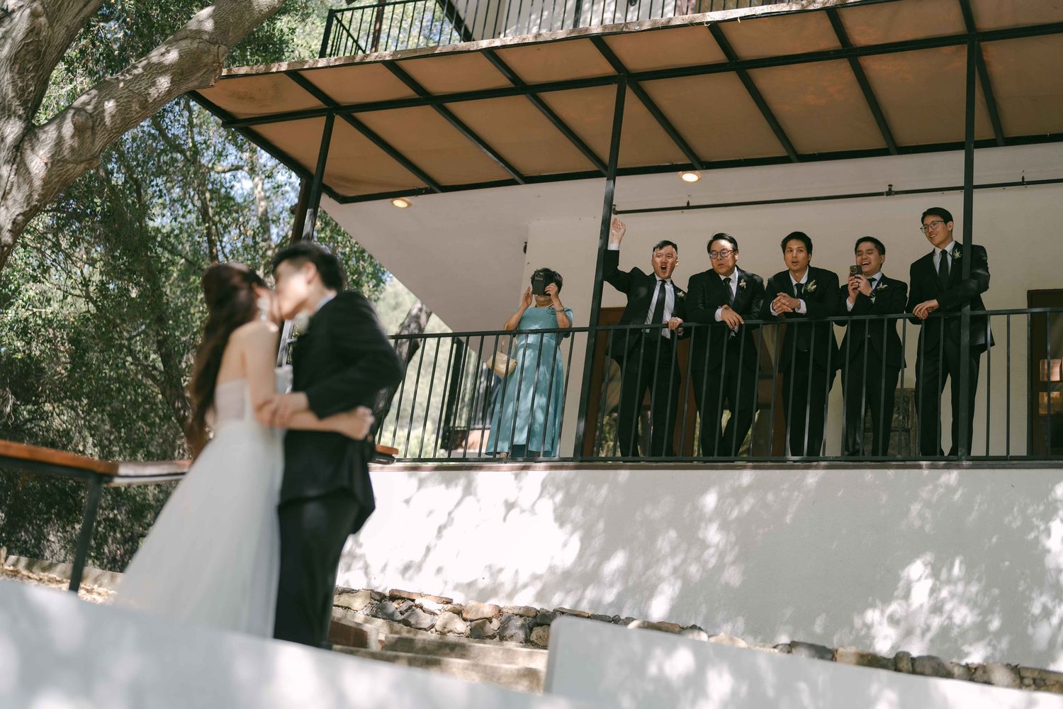 Outdoor wedding ceremony space with guests watching from a covered balcony area.
